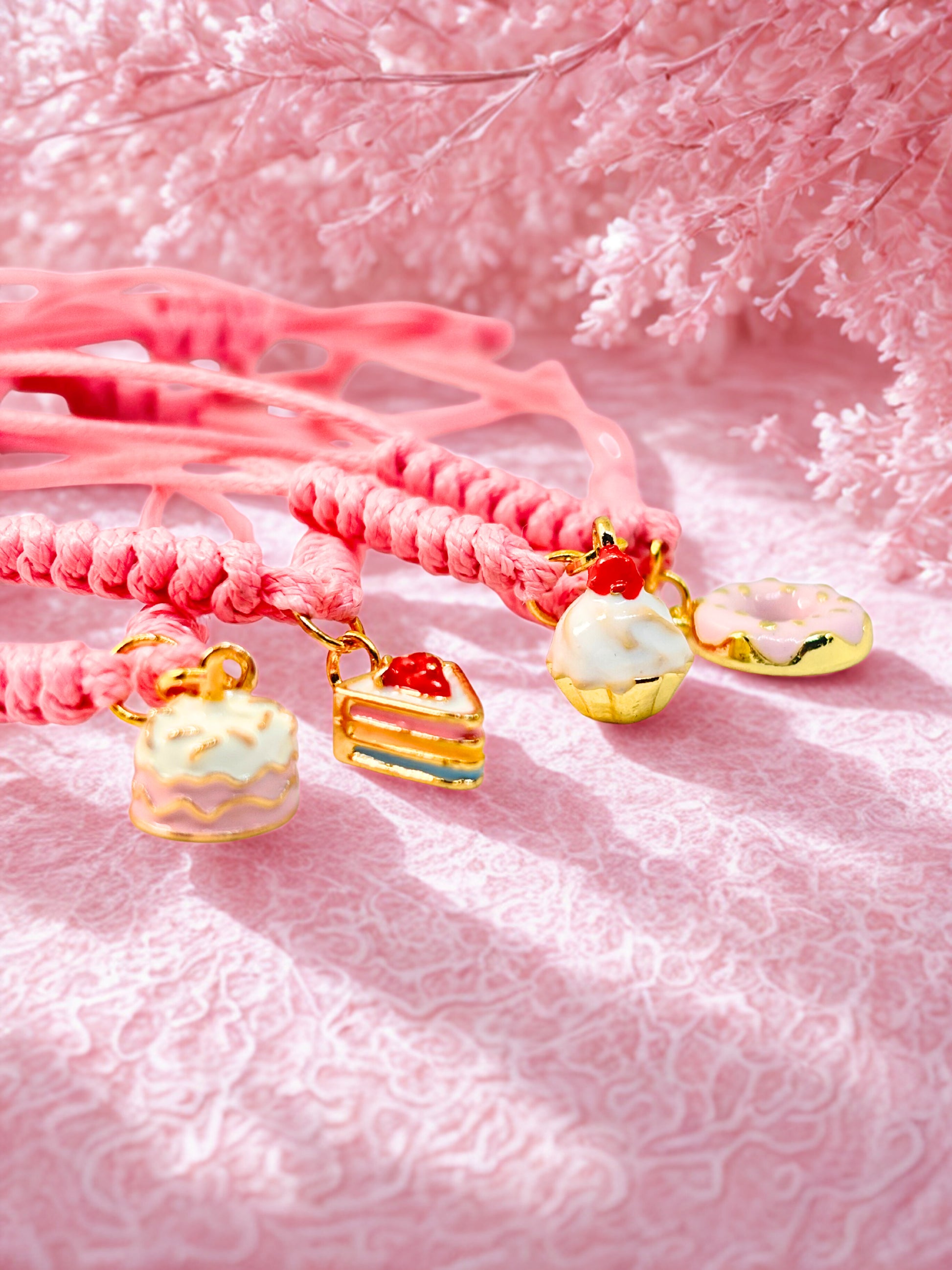 Pink braided bracelets with cake-shaped charms on a pink textured backgrounds 