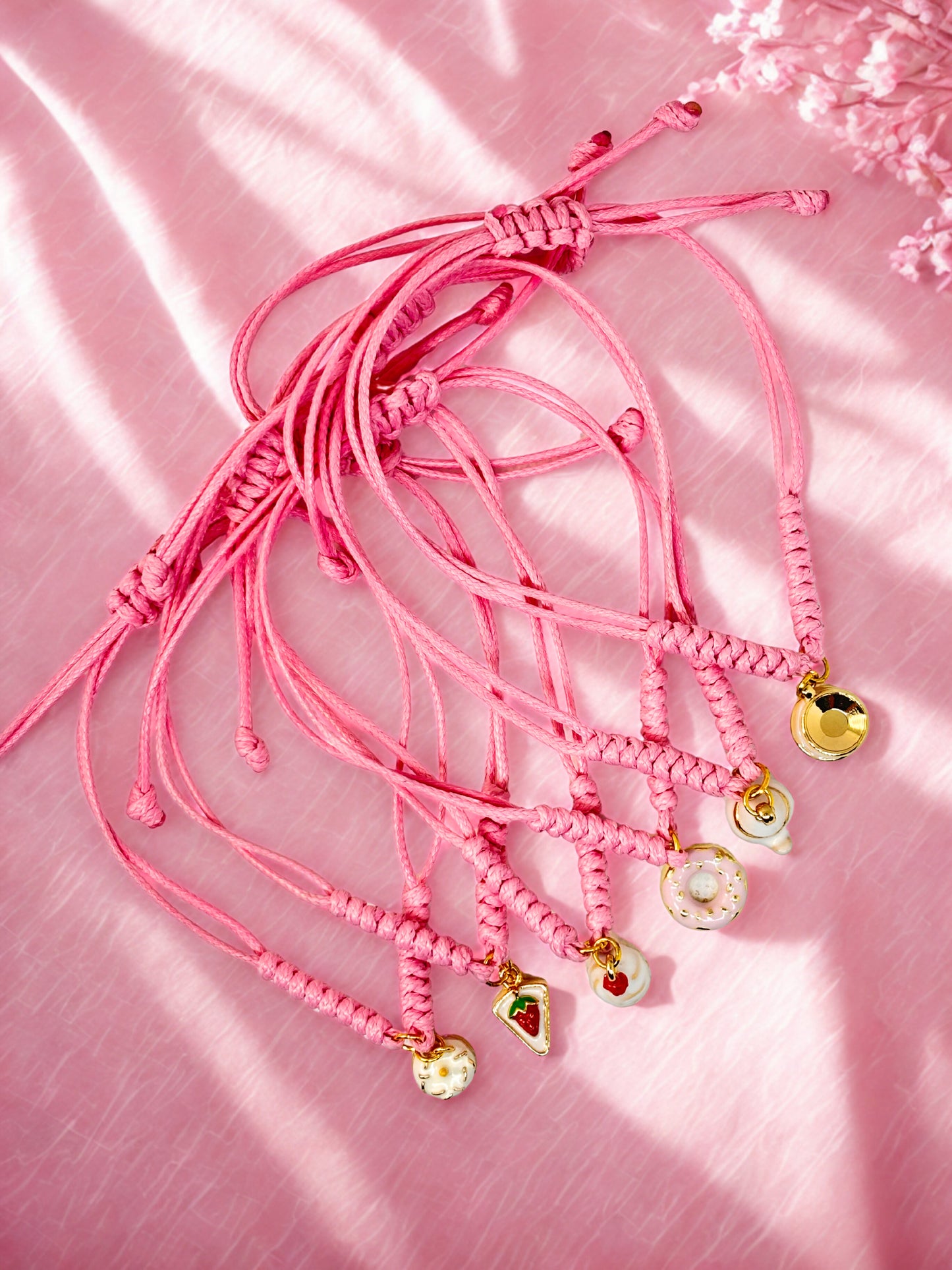 Pink bracelets with gold cake inspired charms on a pink fabric background