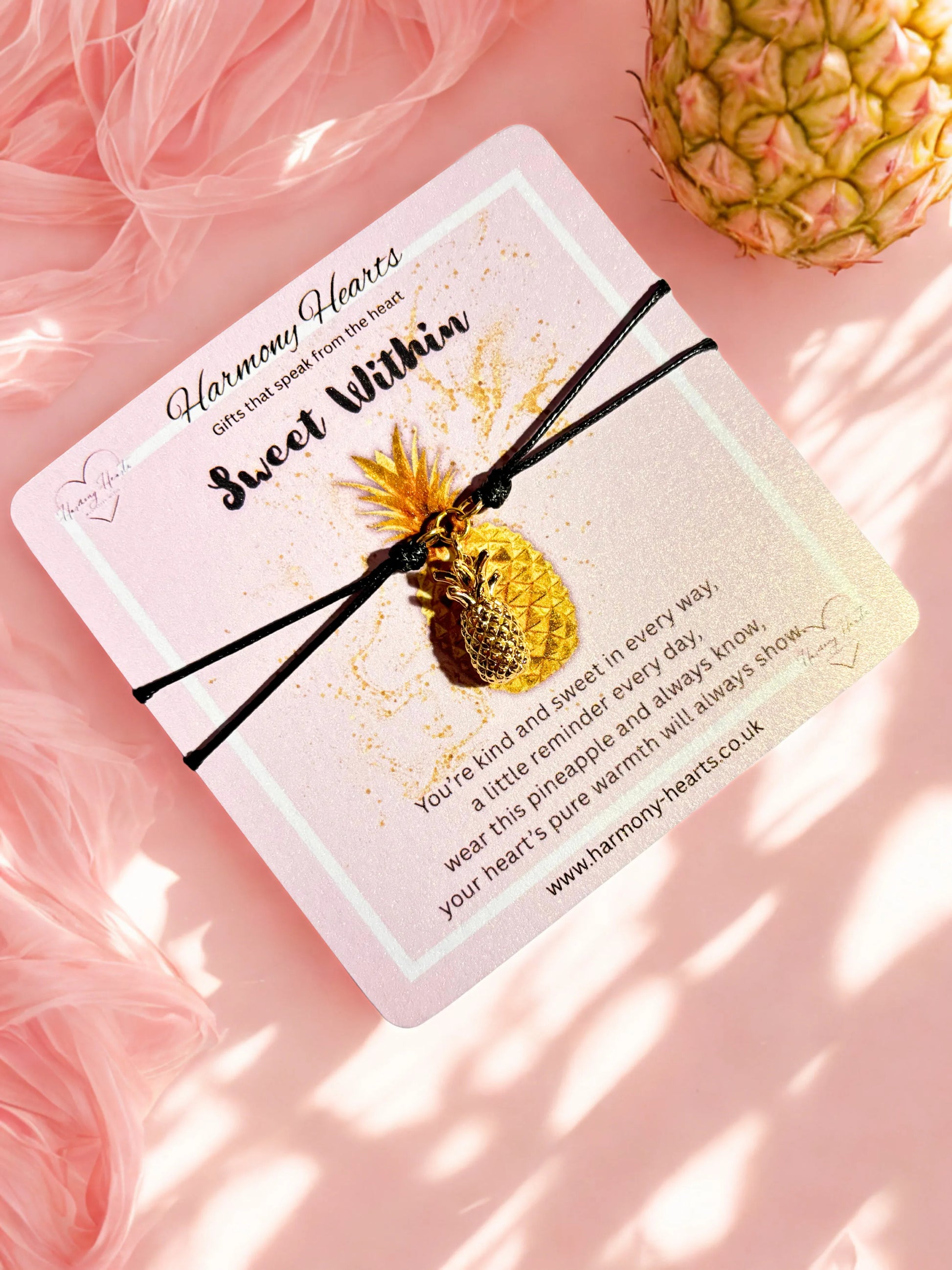 Pineapple-shaped charm on a card with 'Harmony Hearts' branding on a pink fluffy background.