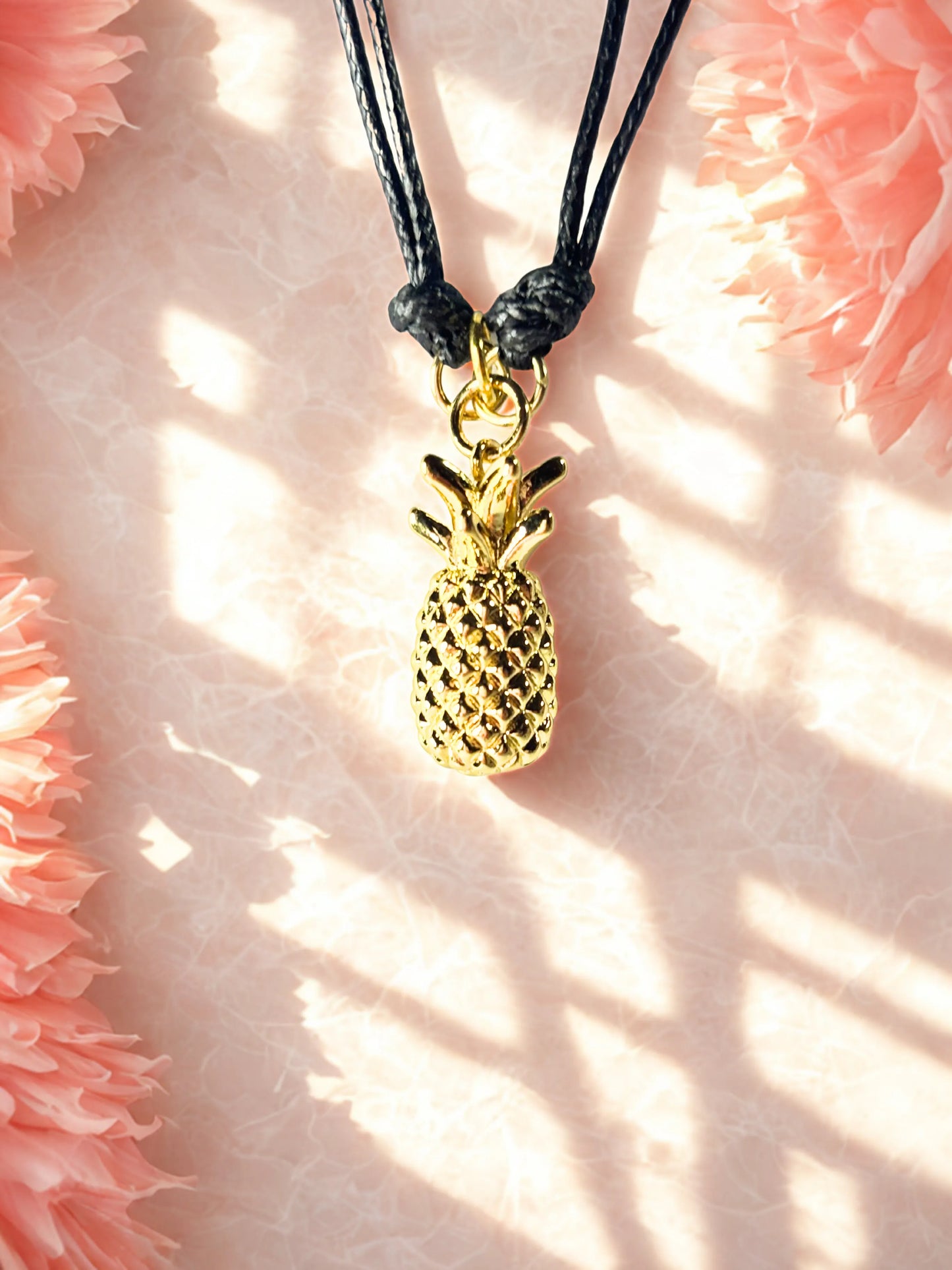Gold pineapple charm on a black cord against a pink floral background