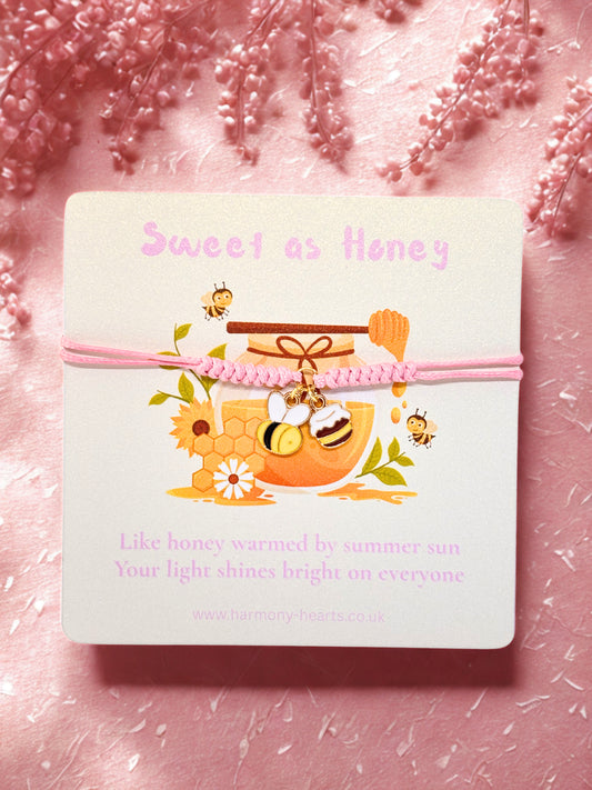 Pink cord bracelet with bee and honey pot charm presented on a branded Harmony Hearts card with Sweet as Honey text