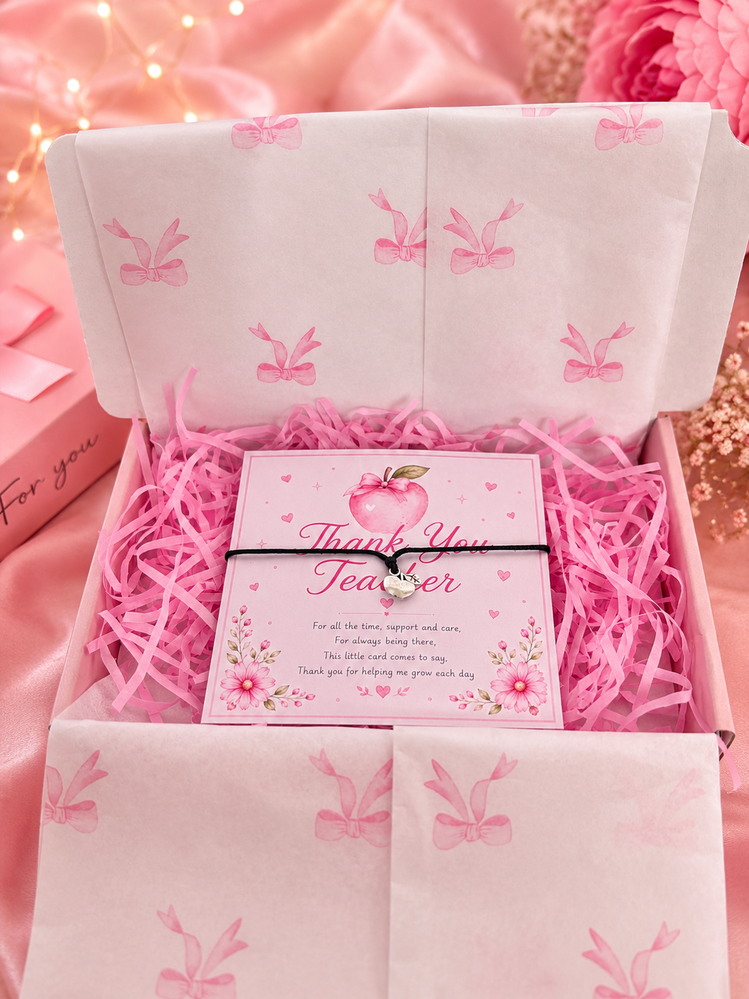 Pink gift box with bracelet and ‘Thank You Teacher' card and decorative elements on a pink background.