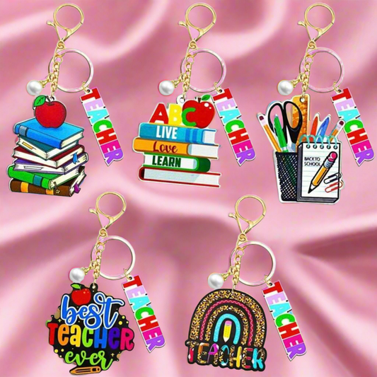 Set of colorful keychains with teacher-themed designs on a pink satin background