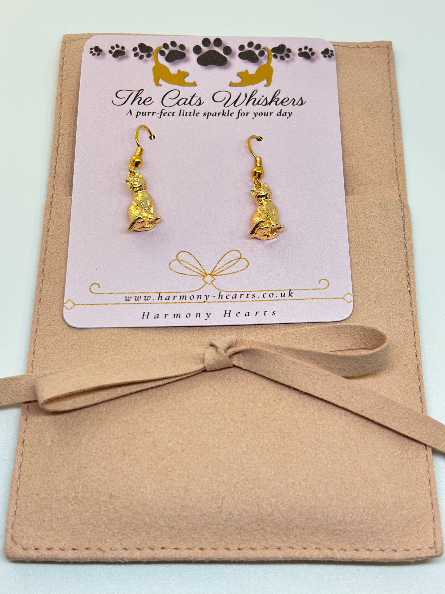 Gold cat-shaped earrings on a 'The Cats Whiskers' branded card with a beige bow.