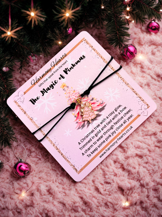 Decorative card with a black cord Christmas tree charm bracelet on a textured surface with Christmas decorations.