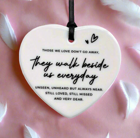 Heart-shaped ceramic ornament with a quote on it, held against a pink fabric background.