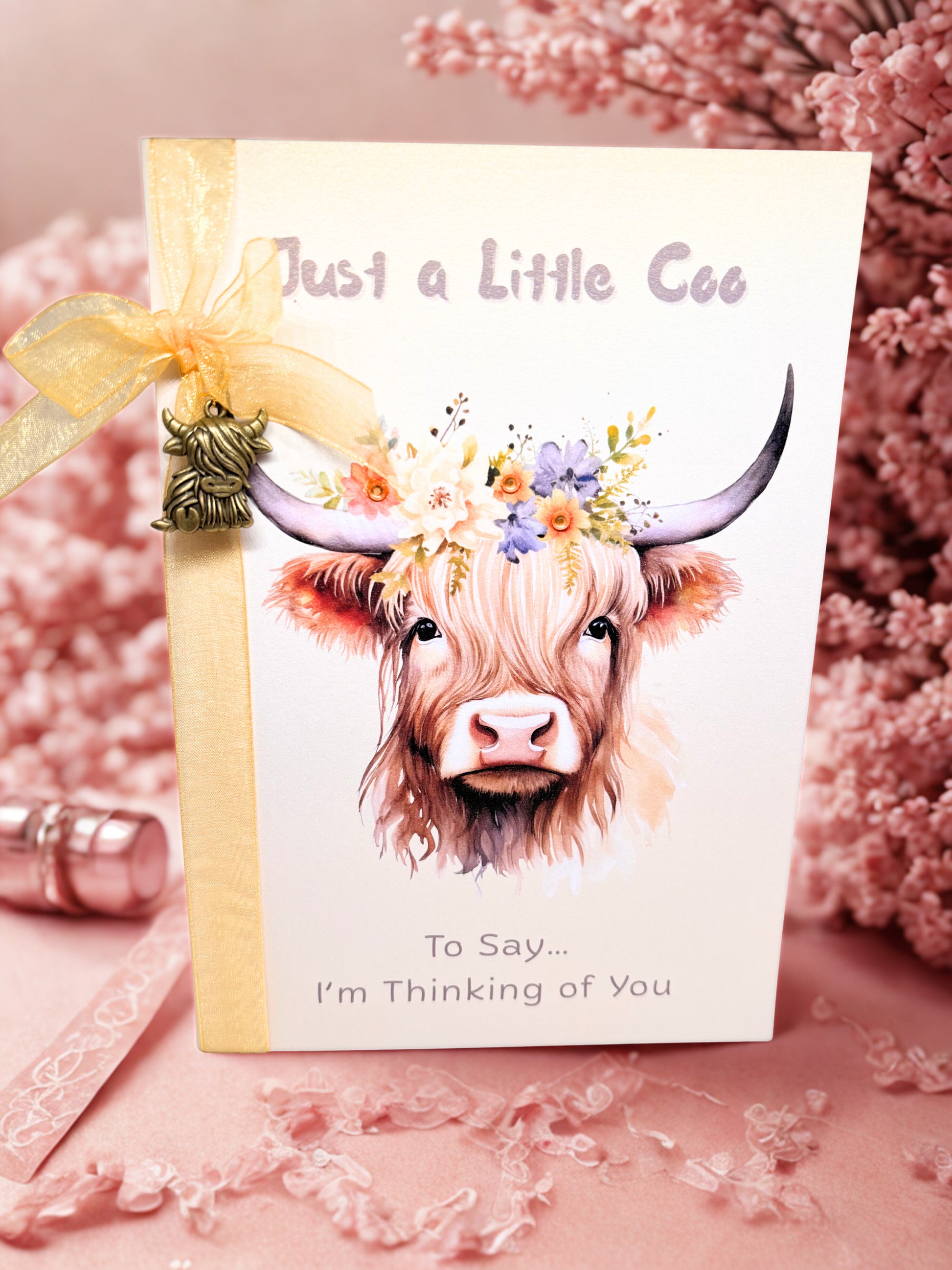 Greeting card with a highland cow illustration and decorative bow on a pink floral background