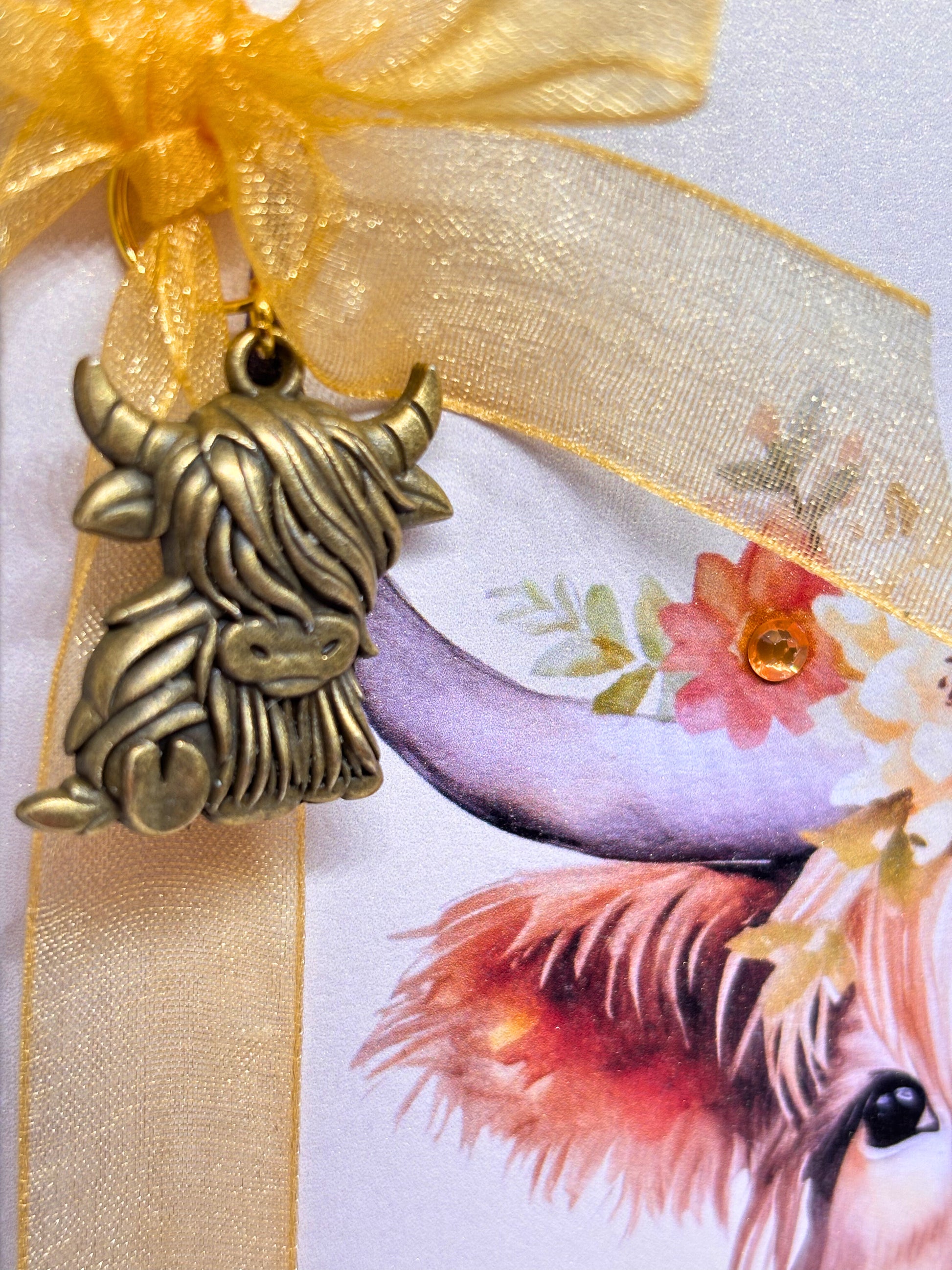 Brass highland cow charm on a yellow ribbon on a greeting card with a floral background