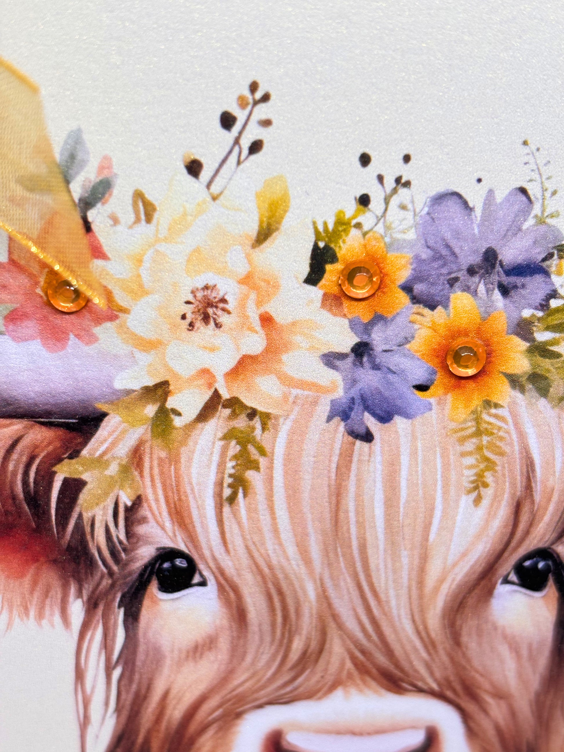 Close-up of a highland cow head with rhinestones with a floral wreath on a light background