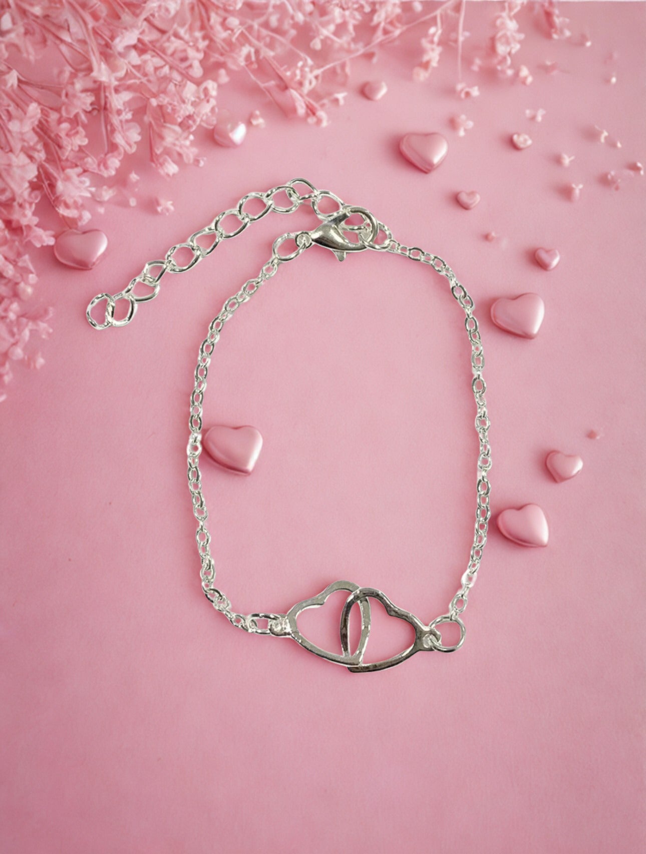 Silver bracelet with heart design on a pink background with heart-shaped objects