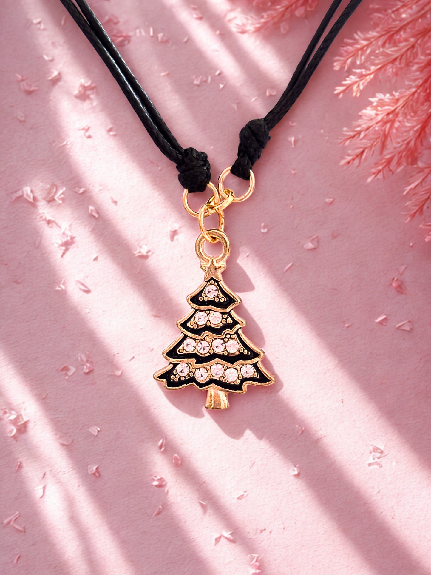 Black and gold Christmas tree charm bracelet against a pink background