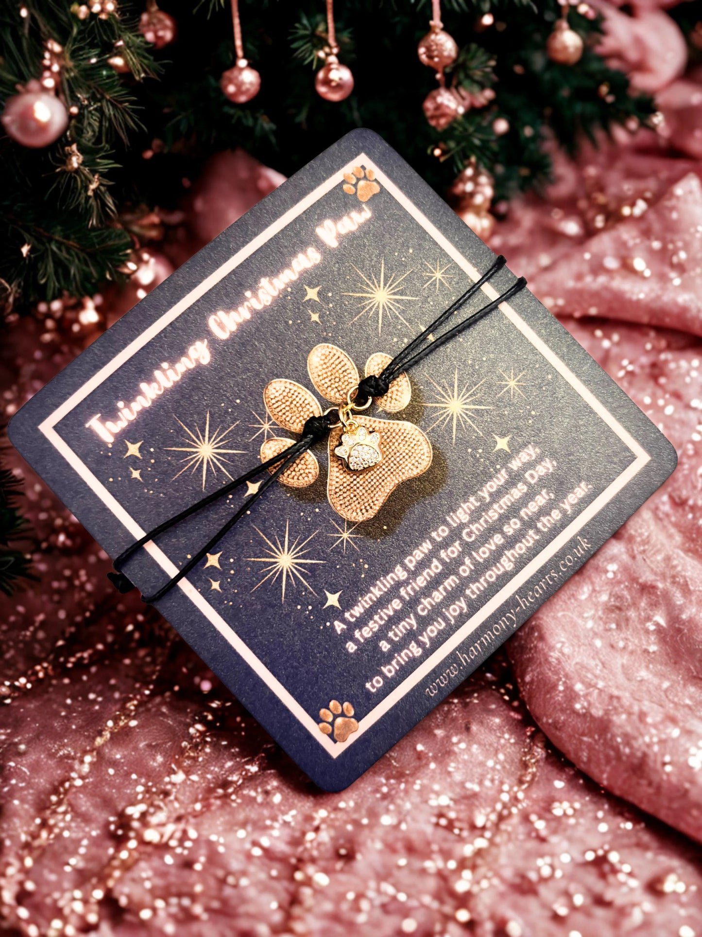 Gold paw-shaped charm bracelet on a black cord with decorative packaging against a festive background.