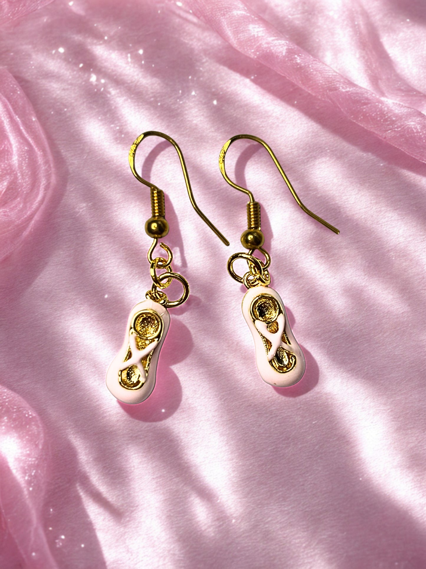 Gold and pink ballet shoe earrings on a pink fabric background