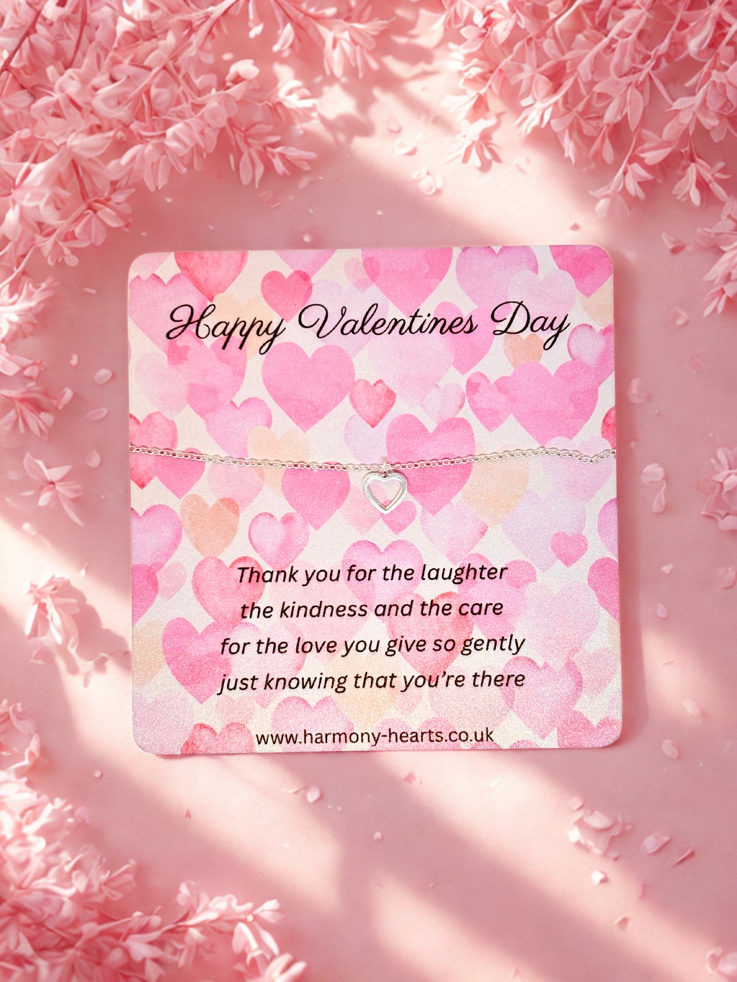 Valentine's Day card with pink heart pattern and message on a pink floral background with a silver heart bracelet