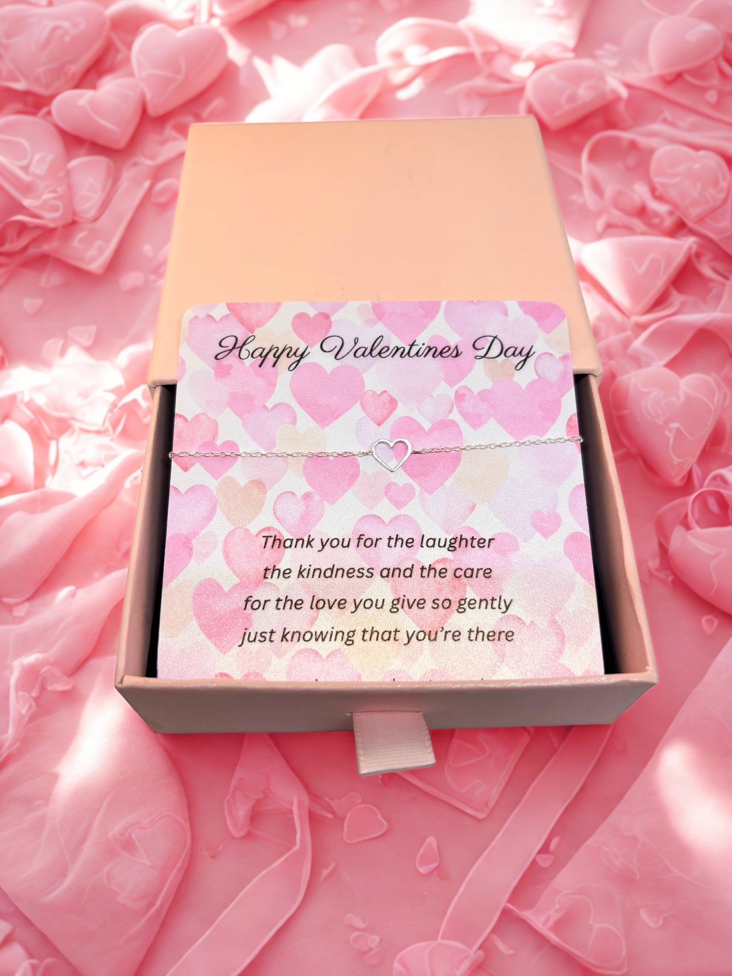 Valentine's Day card in a box with a silver heart bracelet with pink hearts and a message on a pink heart-patterned background.