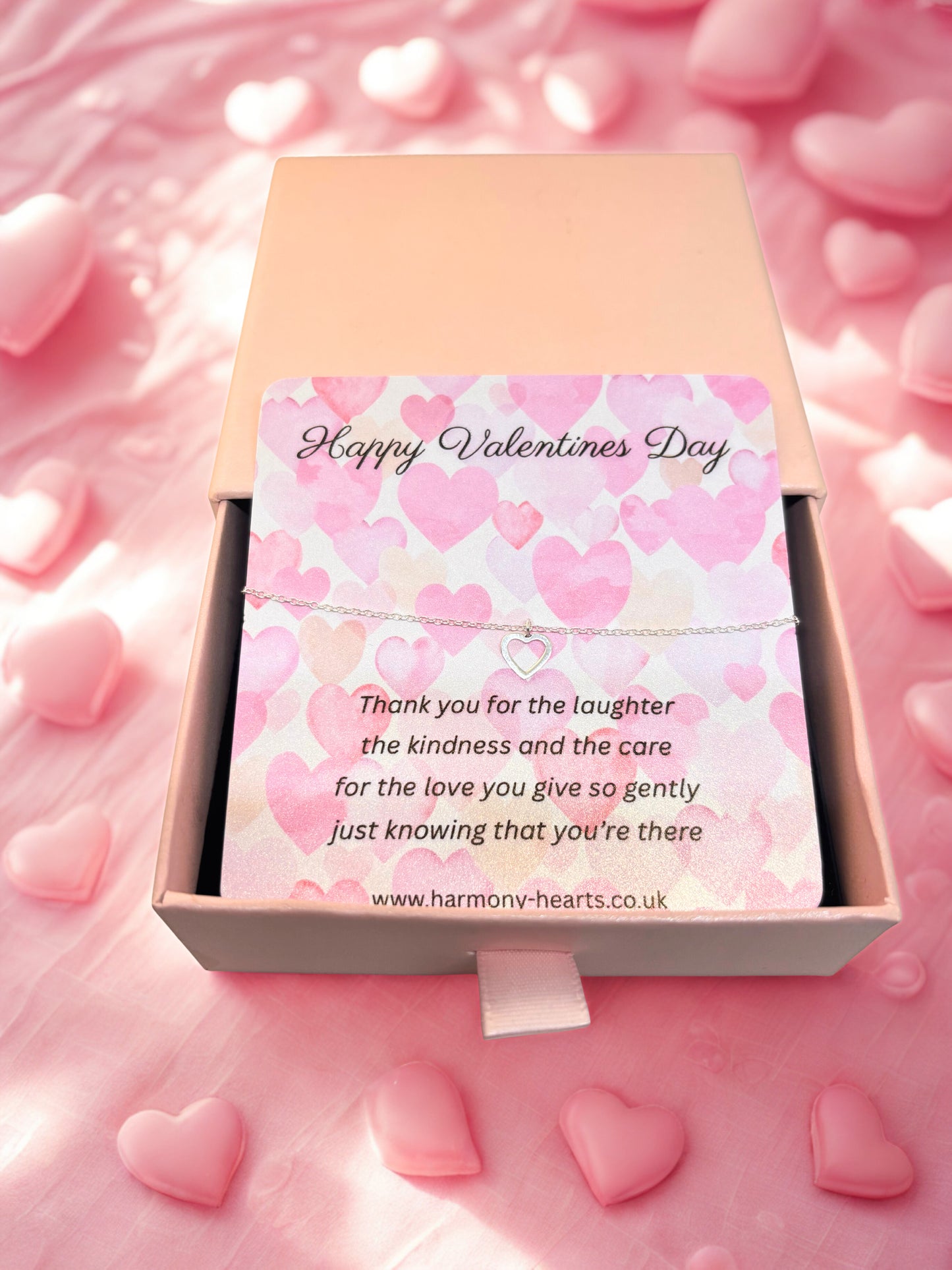 Valentine's Day card with pink hearts and a silver heart bracelet in a box on a pink background
