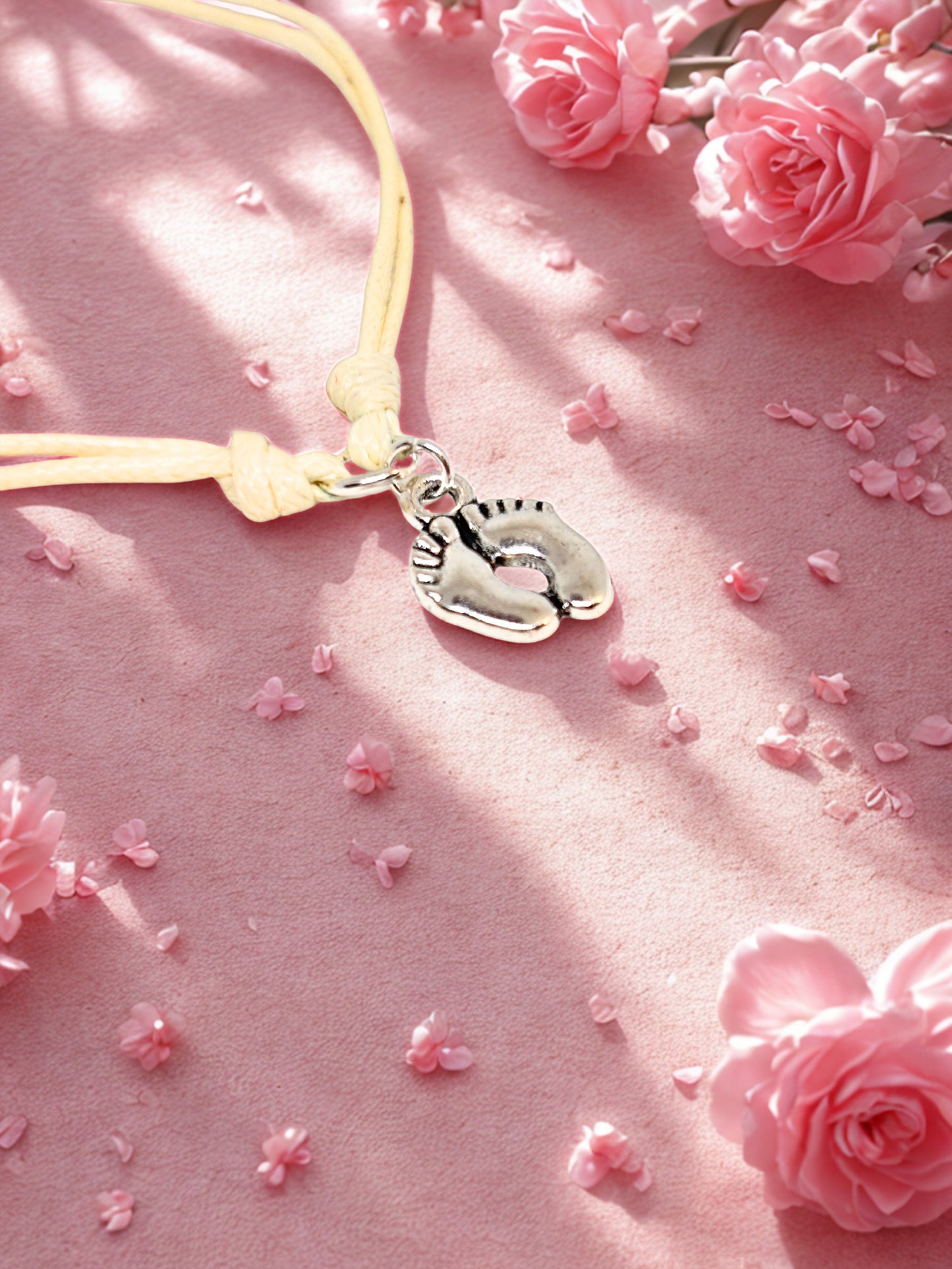 Cord bracelet with a baby feet charm on a pink background with flowers