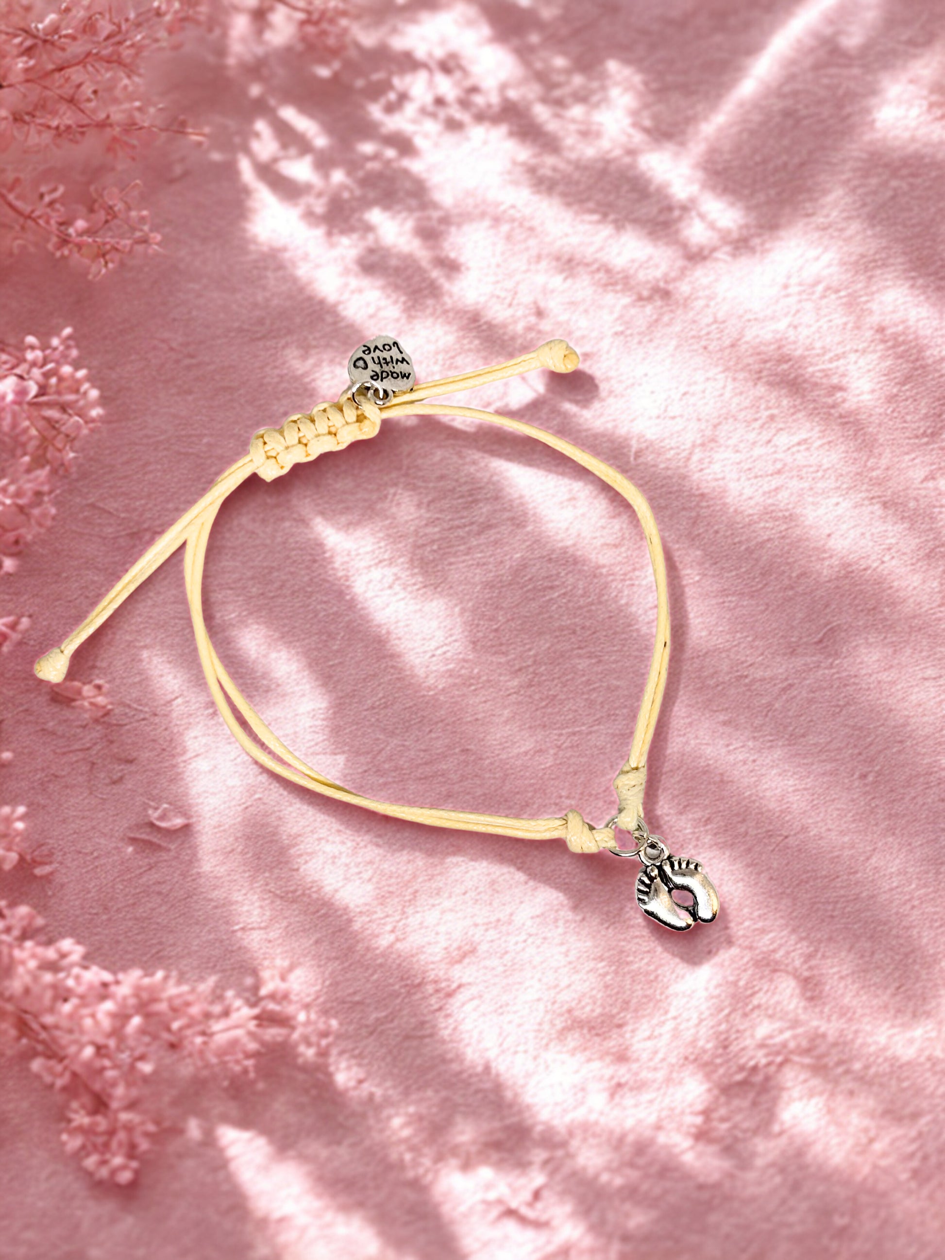 Cord bracelet with a baby feet charm on a pink floral background
