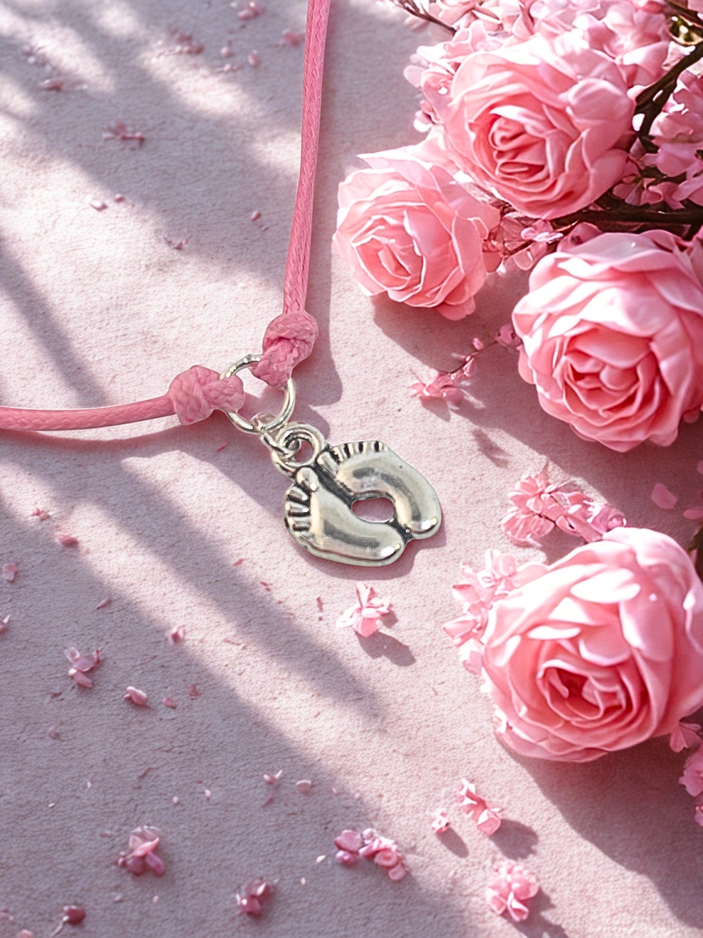 Pink bracelet with a silver charm on a pink surface with pink roses.