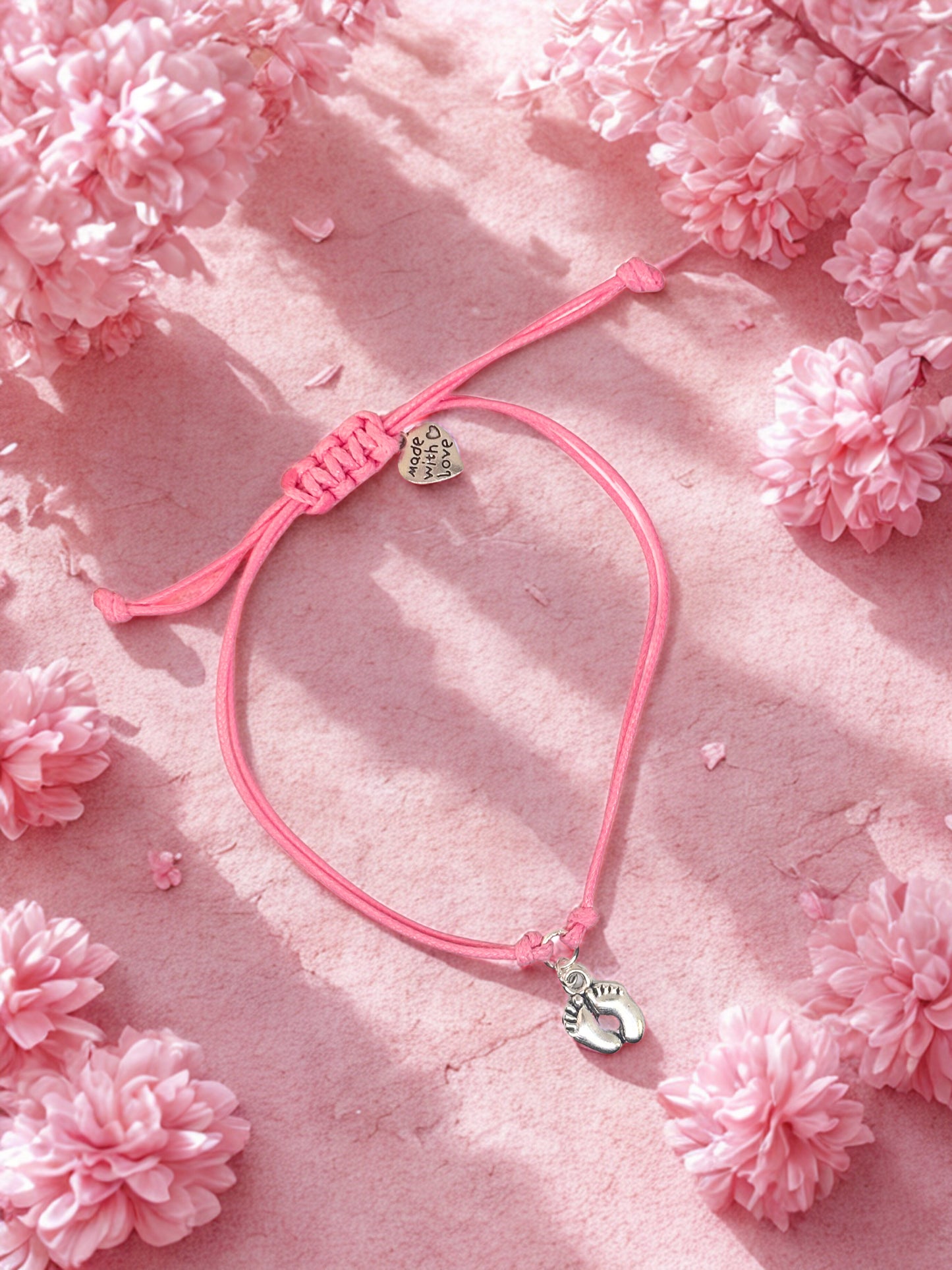 Pink bracelet with heart and foot charm on a pink floral background