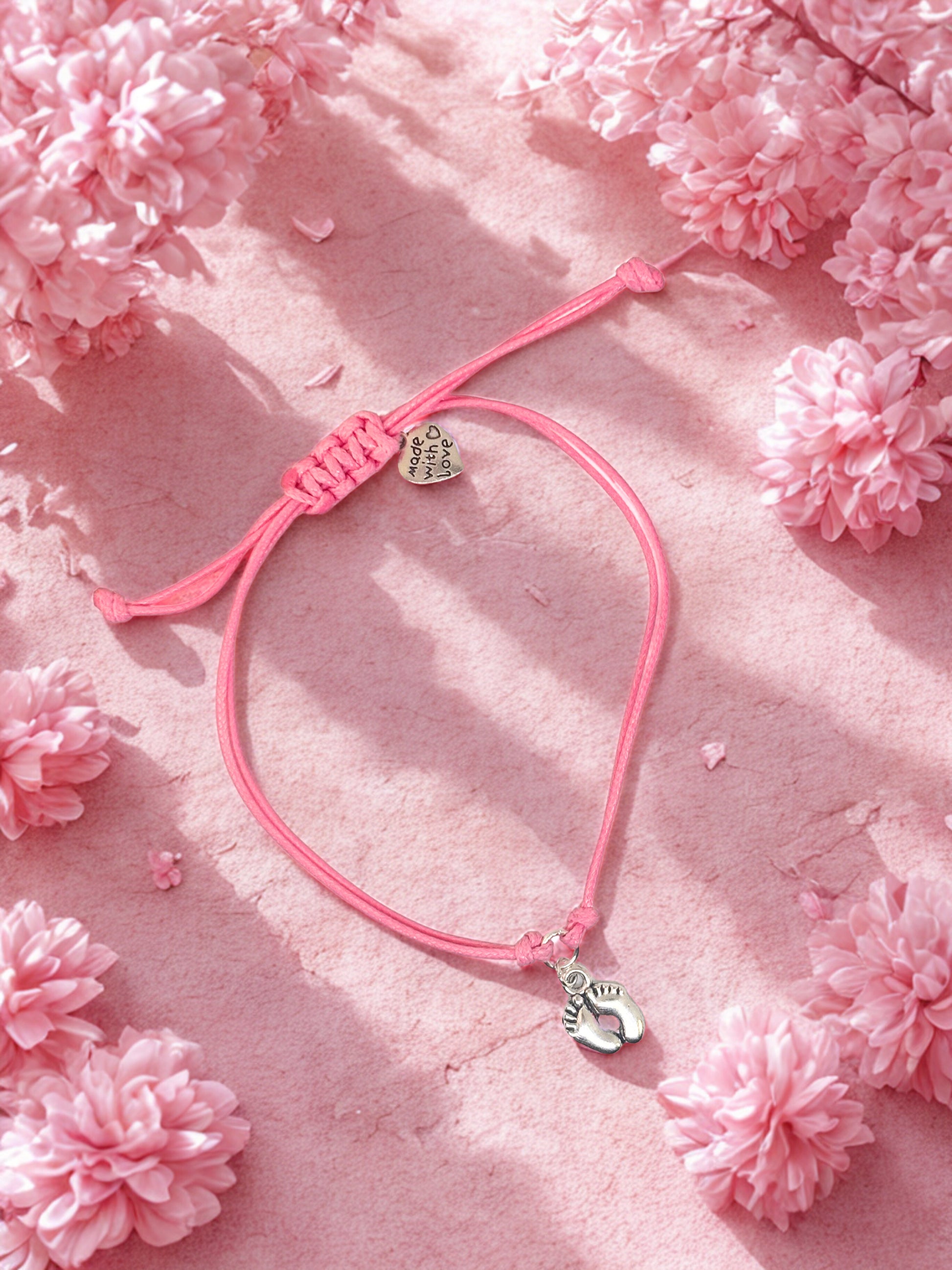 Pink bracelet with heart and foot charm on a pink floral background