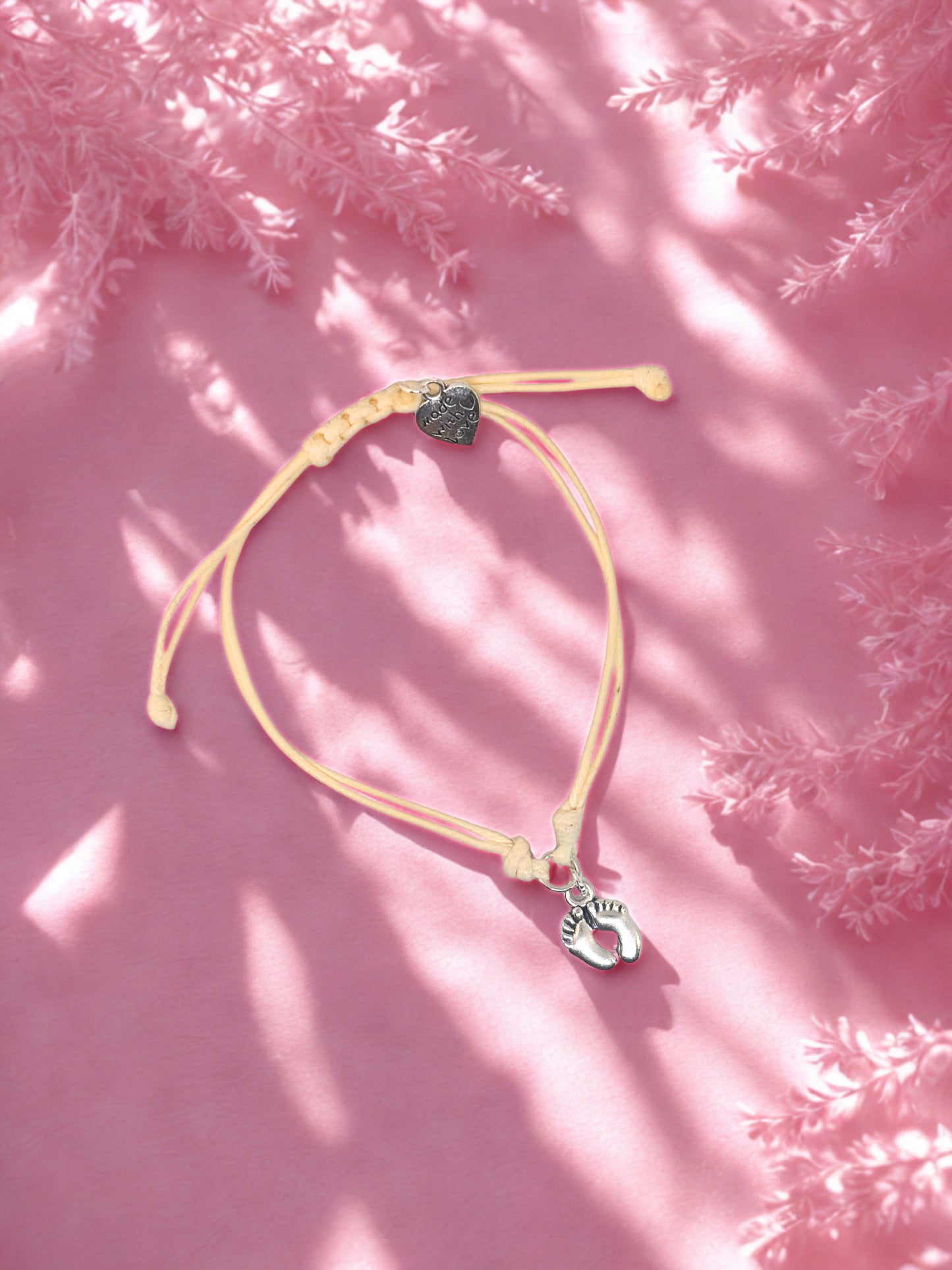 beige charm bracelet with baby feet charms on a pink textured surface