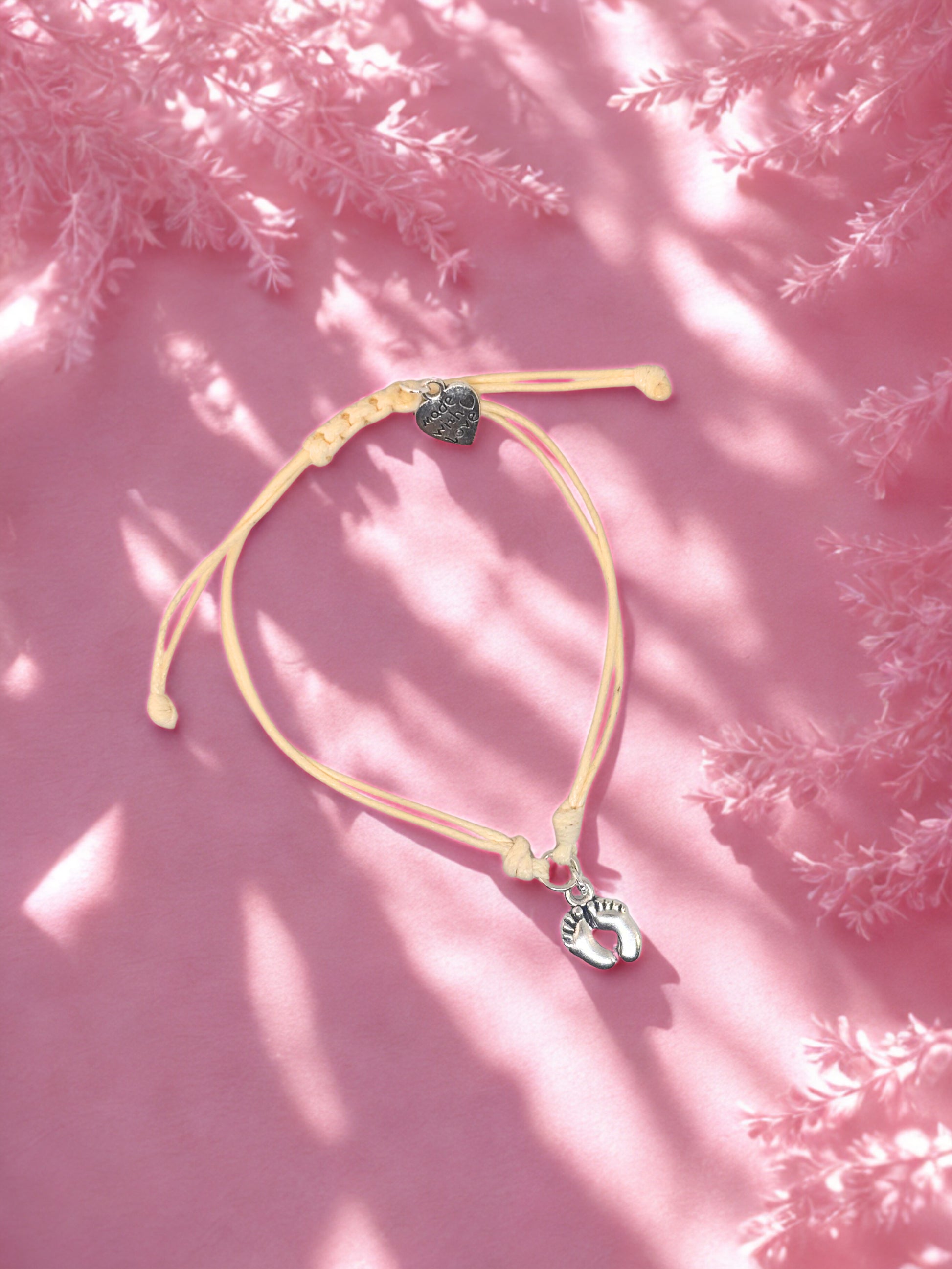 beige charm bracelet with baby feet charms on a pink textured surface