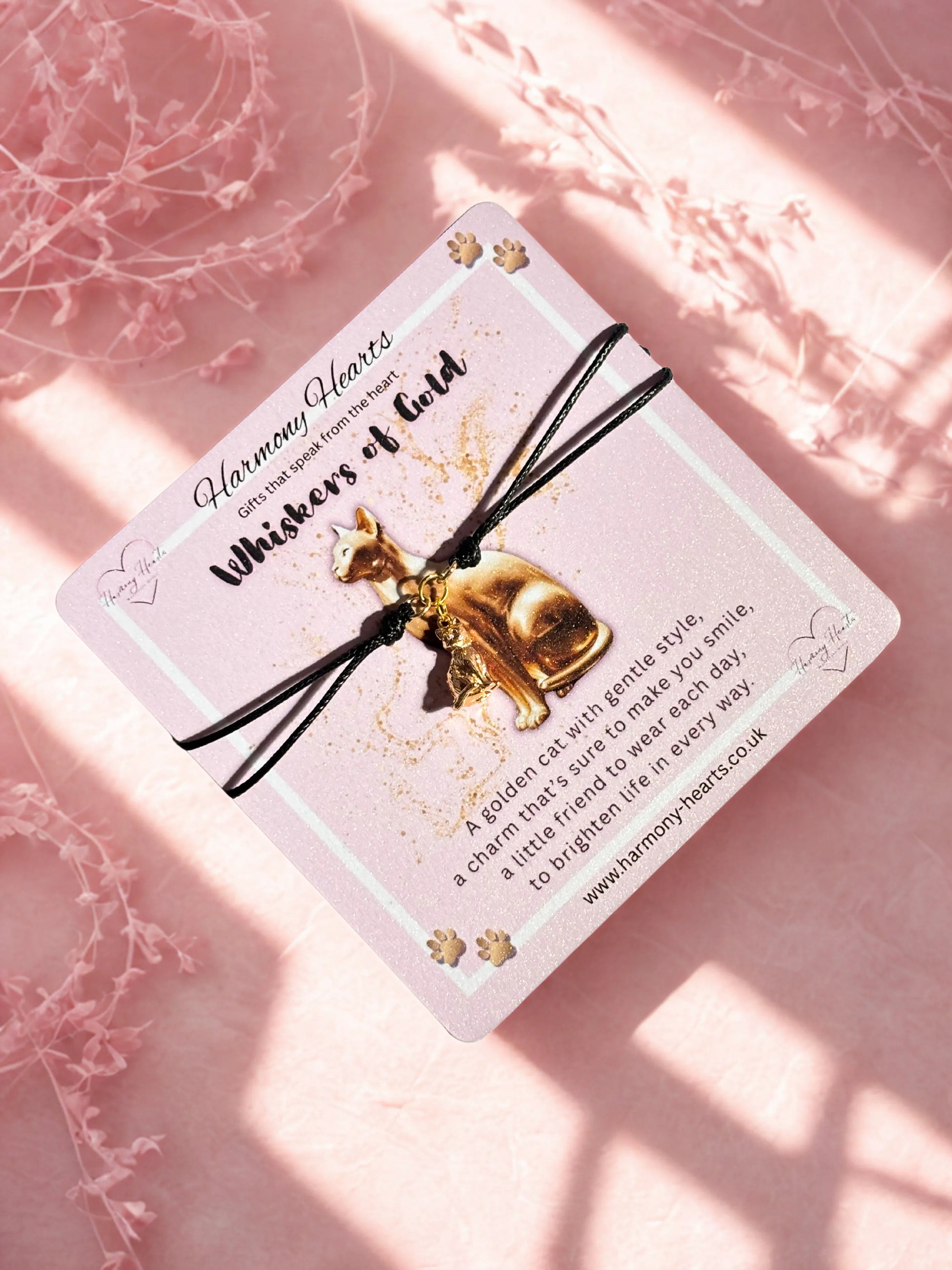 Gold cat charm on a black string with a card on a pink background