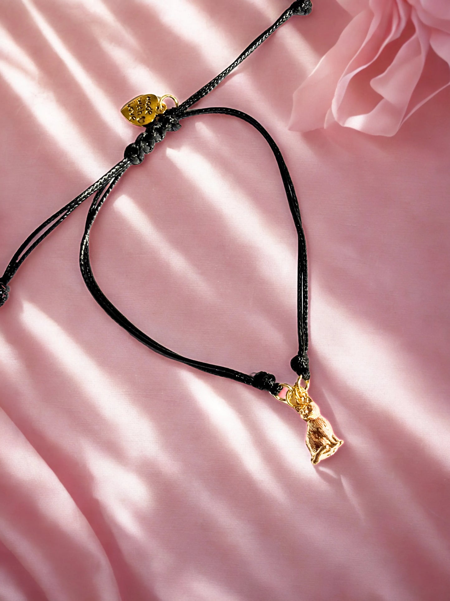 Bracelet with a gold cat charm on a pink background