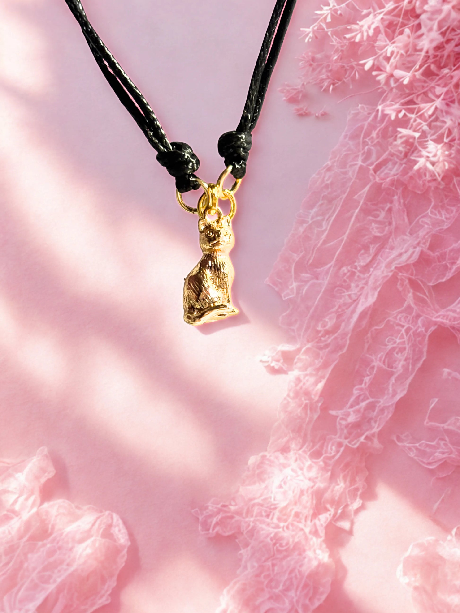 Bracelet with a gold cat charm on a pink textured background