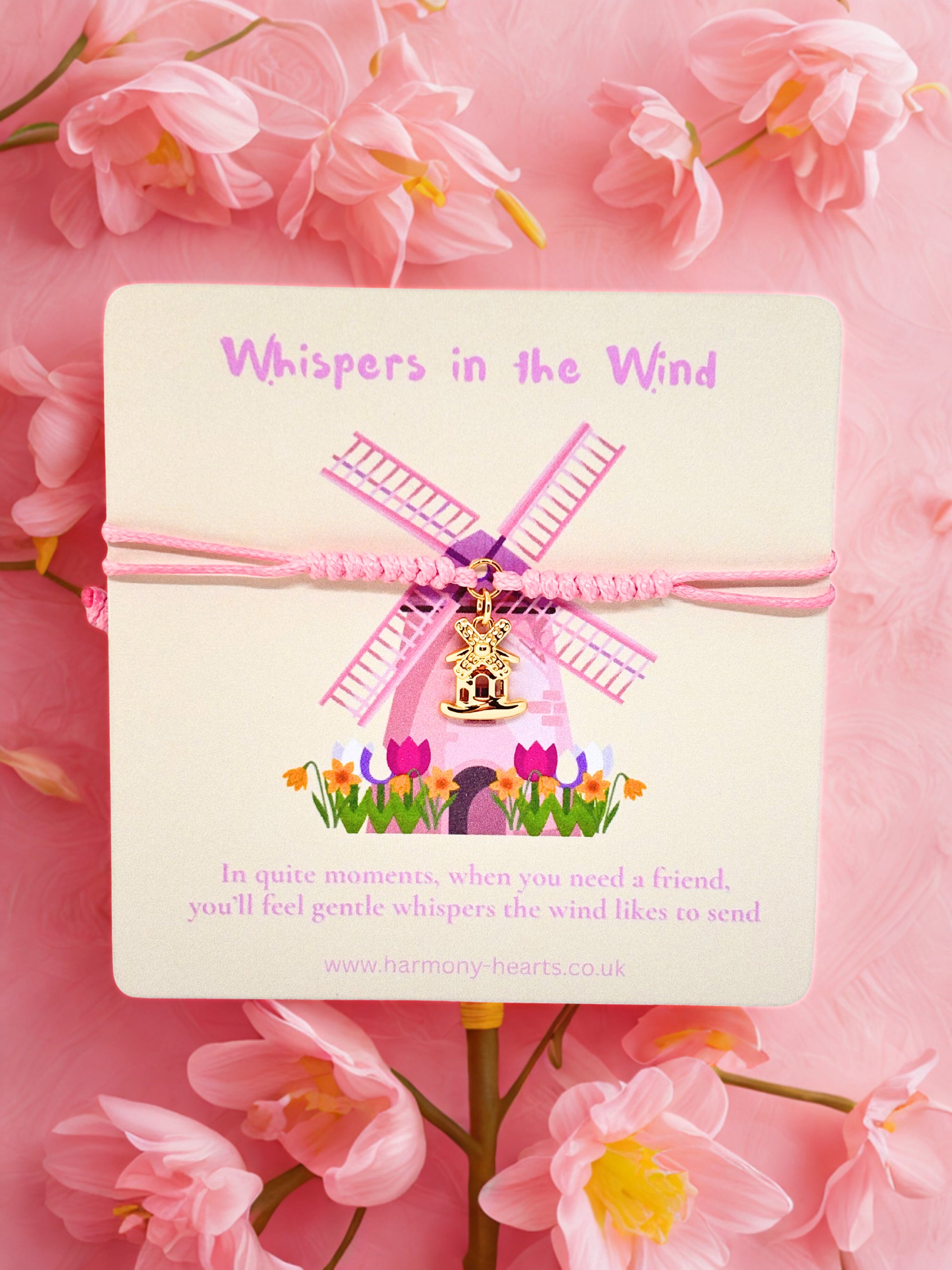 Pink windmill charm on a card with 'Whispers in the Wind' text, surrounded by pink flowers.