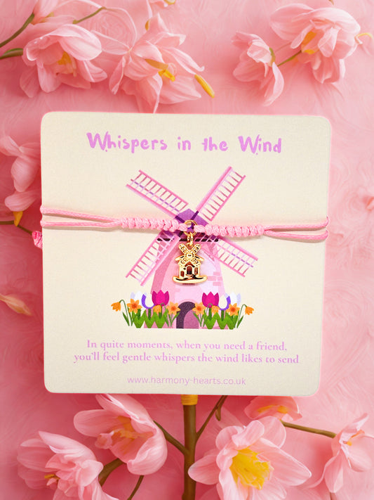 Pink windmill charm on a card with 'Whispers in the Wind' text, surrounded by pink flowers.
