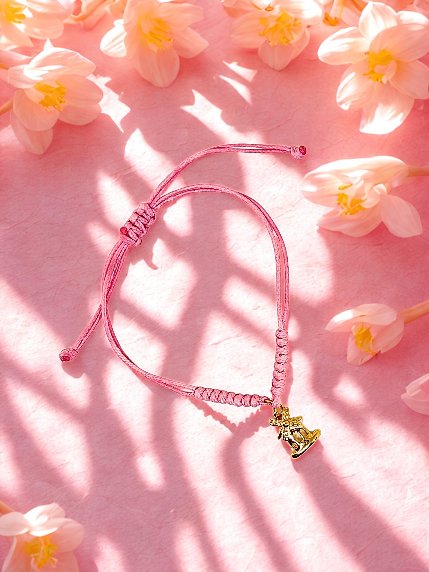 Pink braided bracelet with a gold windmill charm on a pink floral background