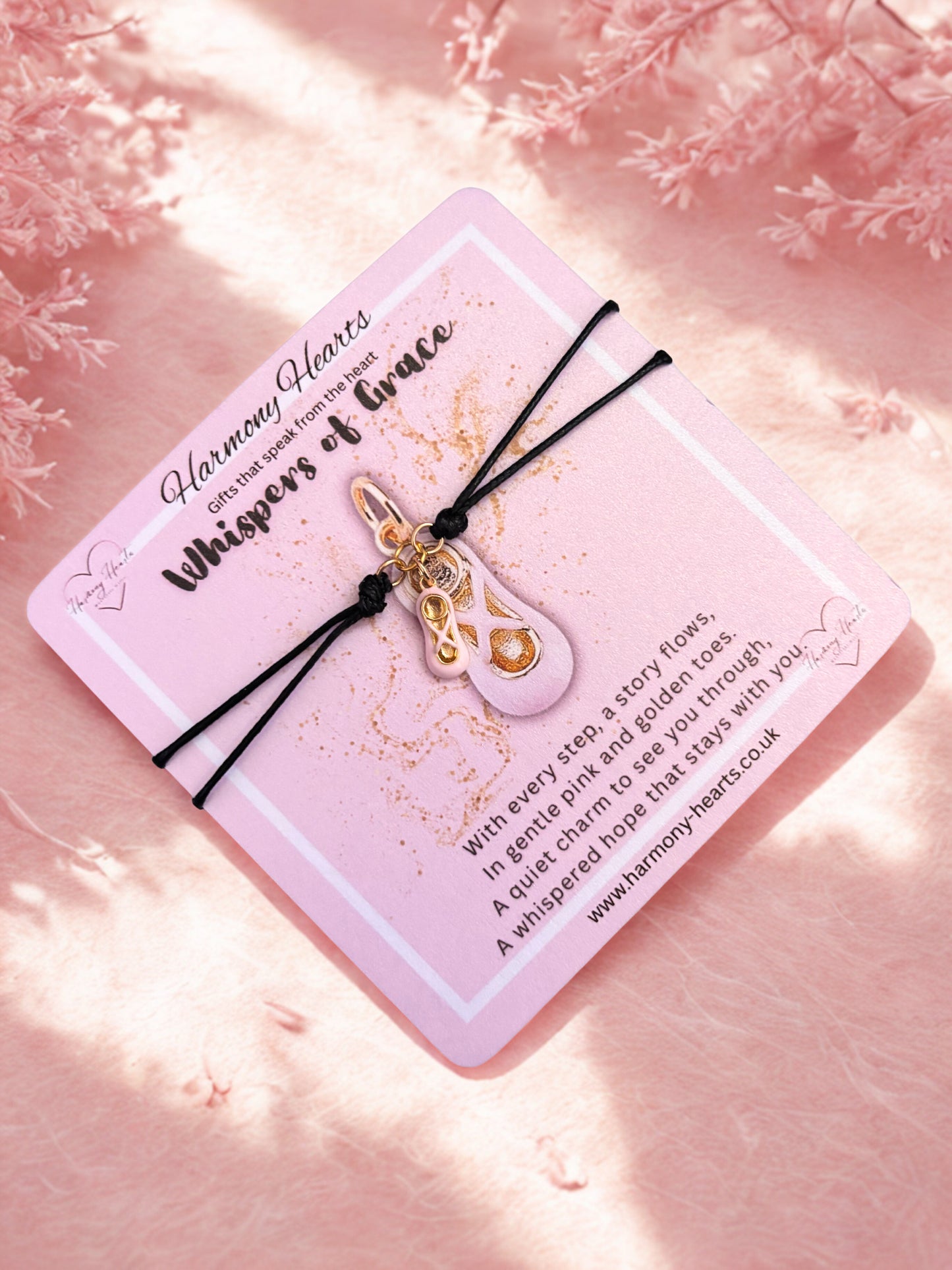 Bracelet with gold and pink ballet shoe charm on a pink card with text, against a soft pink background