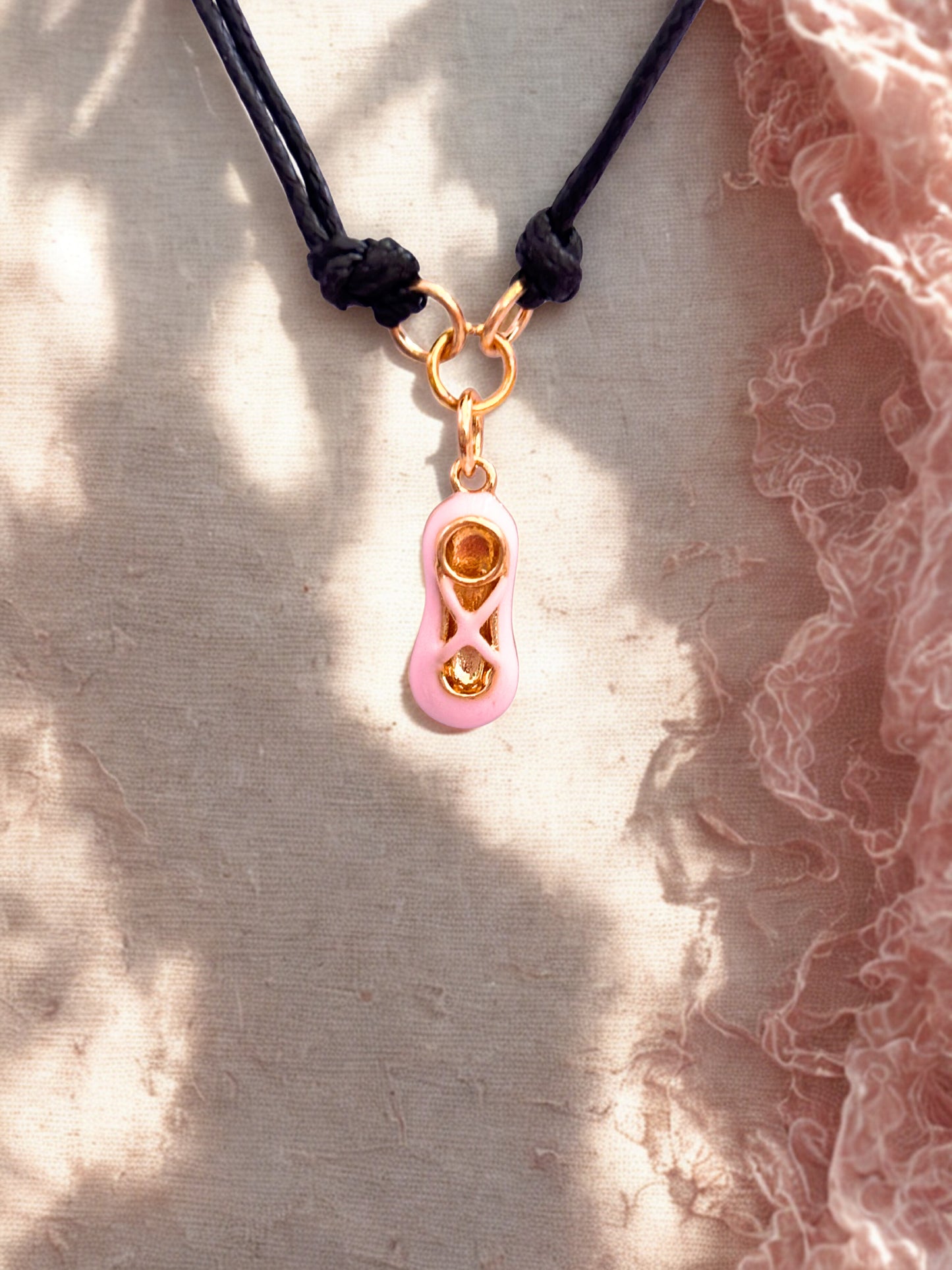 Bracelet with a pink and gold ballet shoe charm on a textured surface