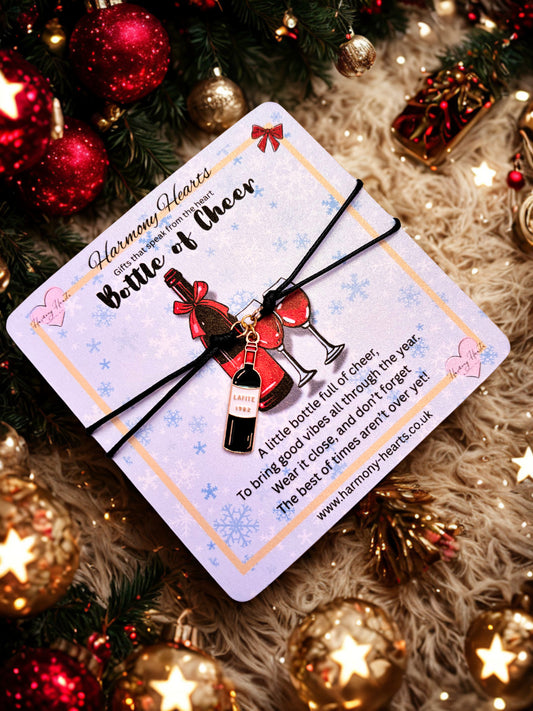 Bottle of Cheer bracelet on a decorative card with Christmas ornaments in the background