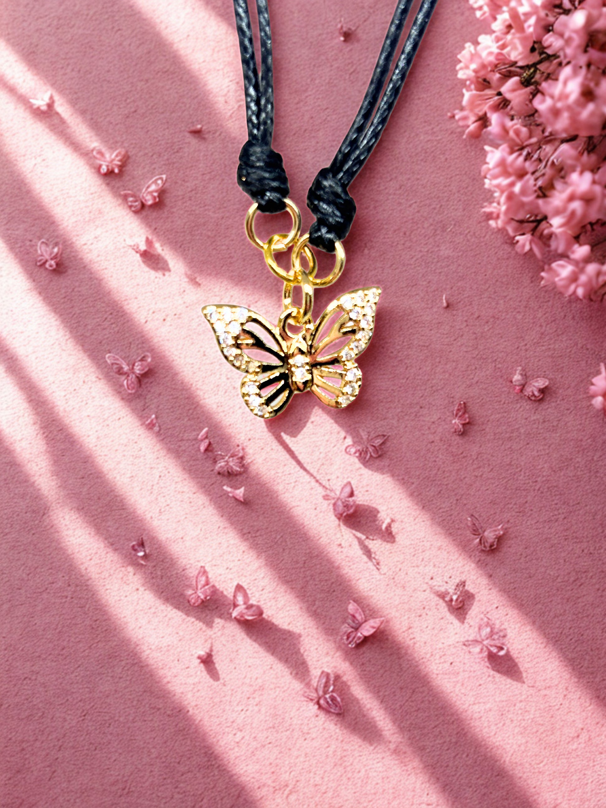 Gold butterfly charm on a black cord against a pink background with small flowers.