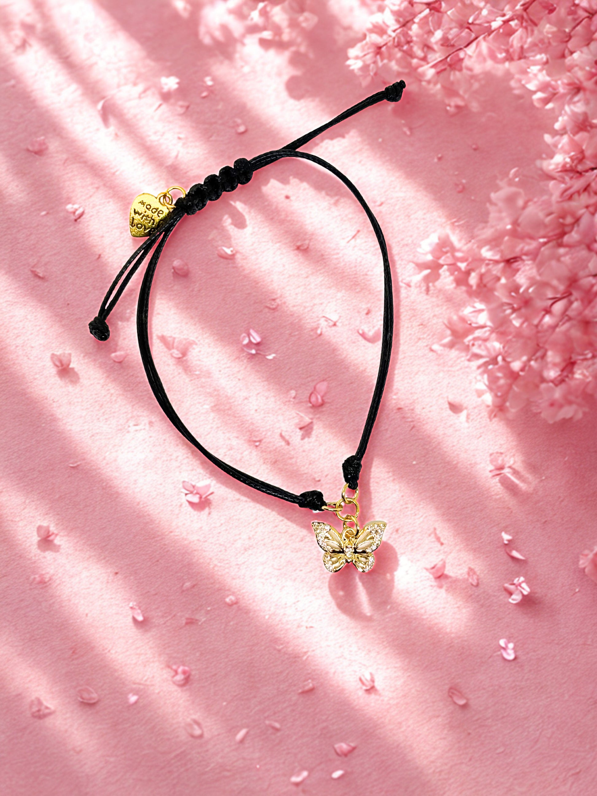 Black cord bracelet with gold butterfly charms on a pink fabric background