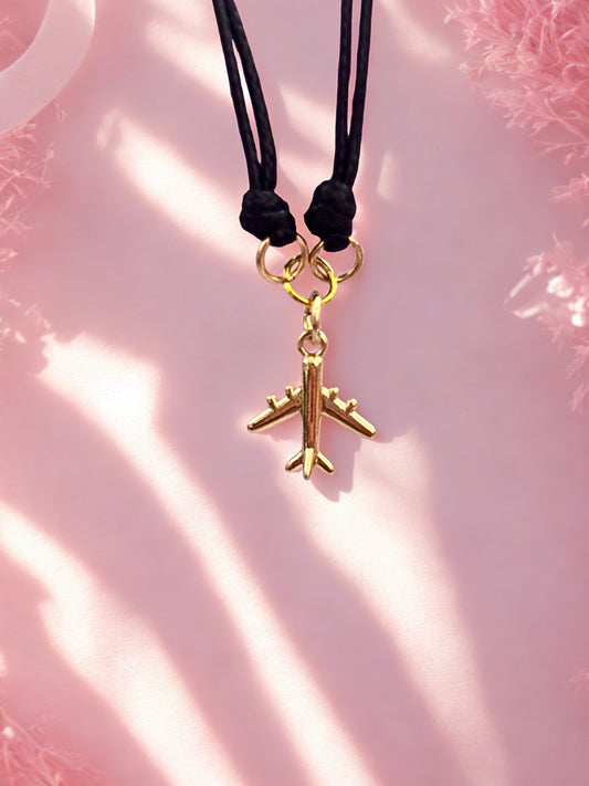 Gold airplane charm on a black cord against a pink background
