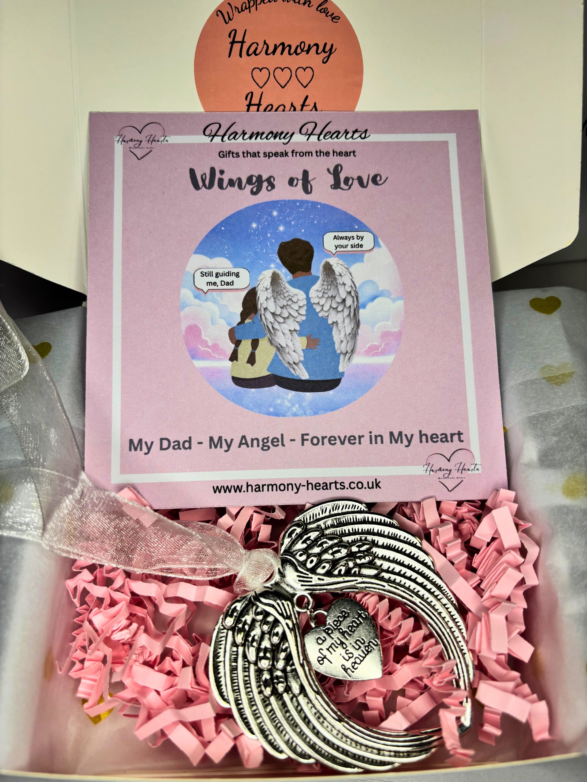 Wings of Love ornament in a box with pink tissue paper and Harmony Hearts packaging.