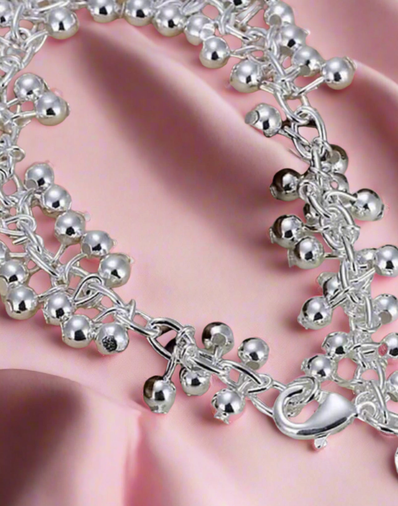 Silver bracelet with bell charms on a pink fabric background