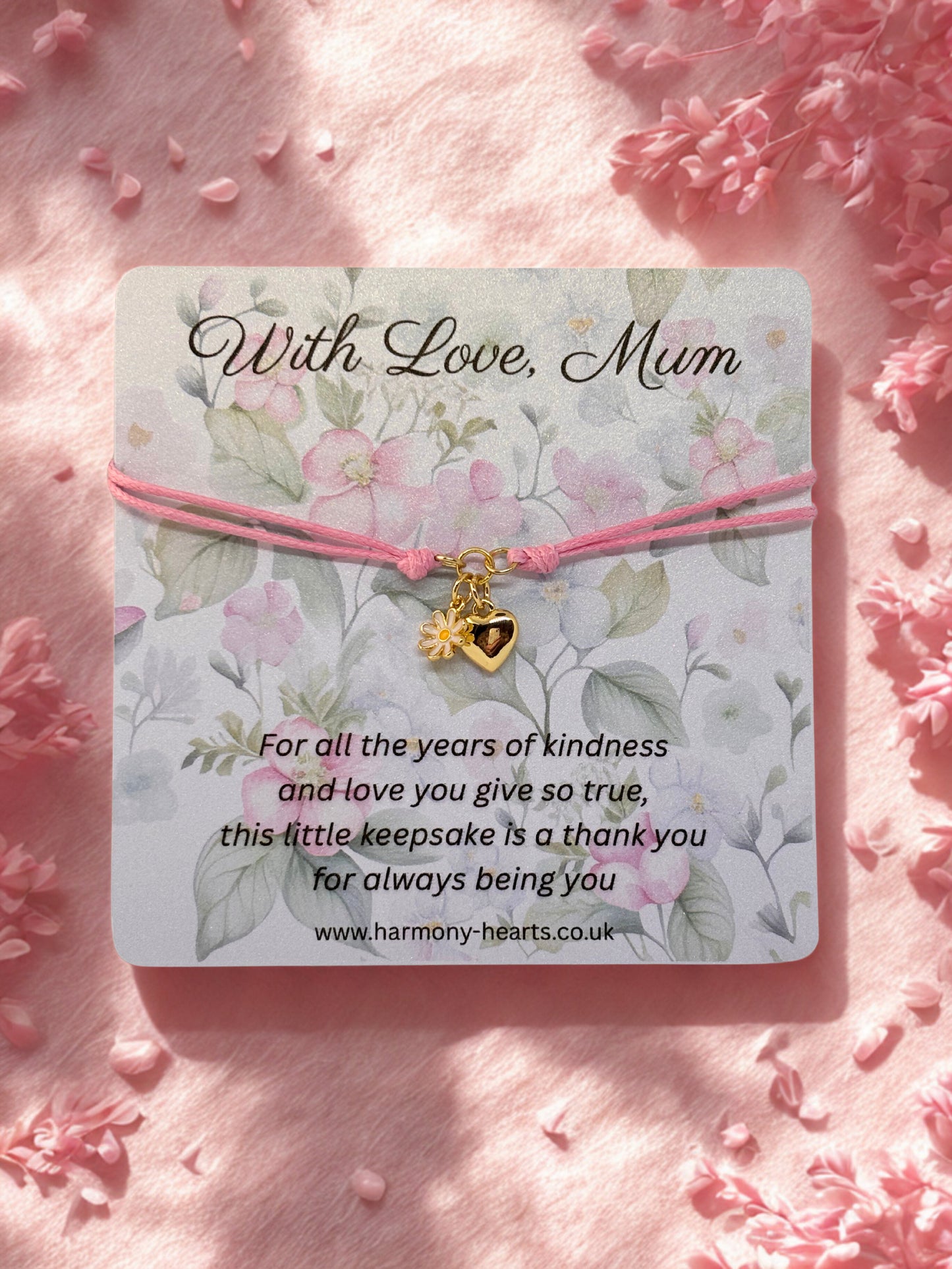 Bracelet with heart and daisy charm on a floral card with 'With Love, Mum' text, surrounded by pink flowers.