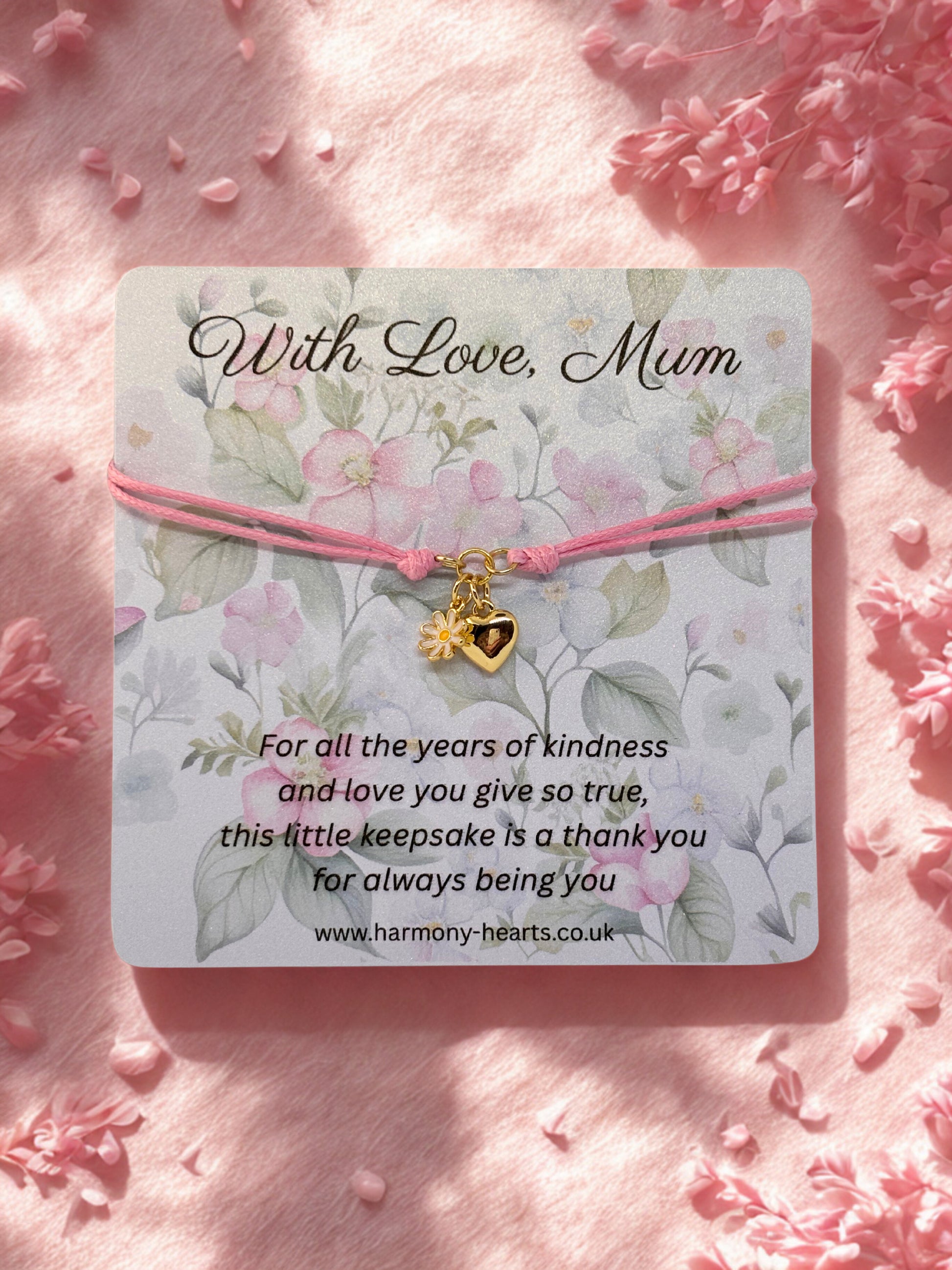 Bracelet with heart and daisy charm on a floral card with 'With Love, Mum' text, surrounded by pink flowers.