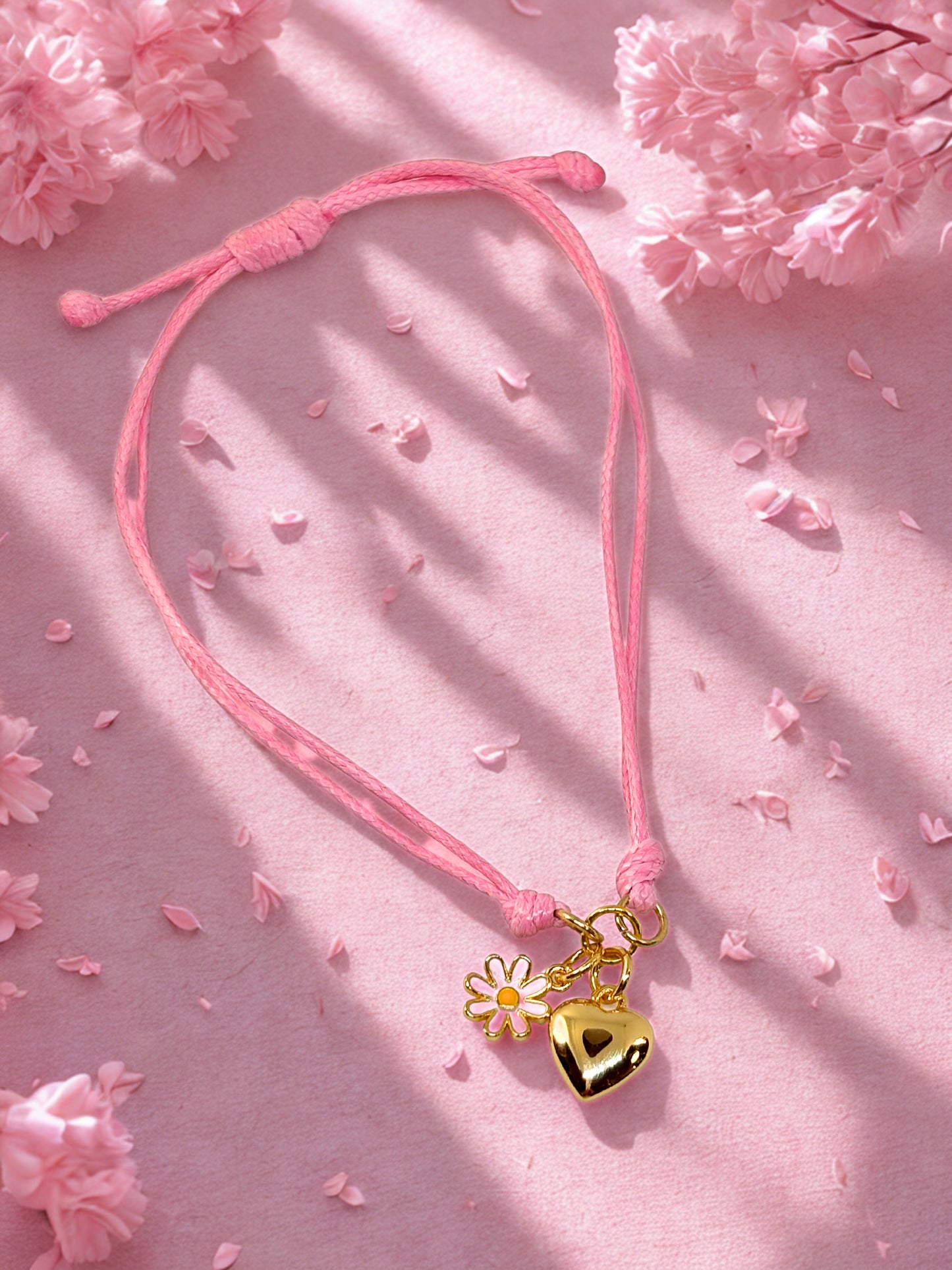 Pink cord bracelet with gold heart and flower charm on a pink floral background