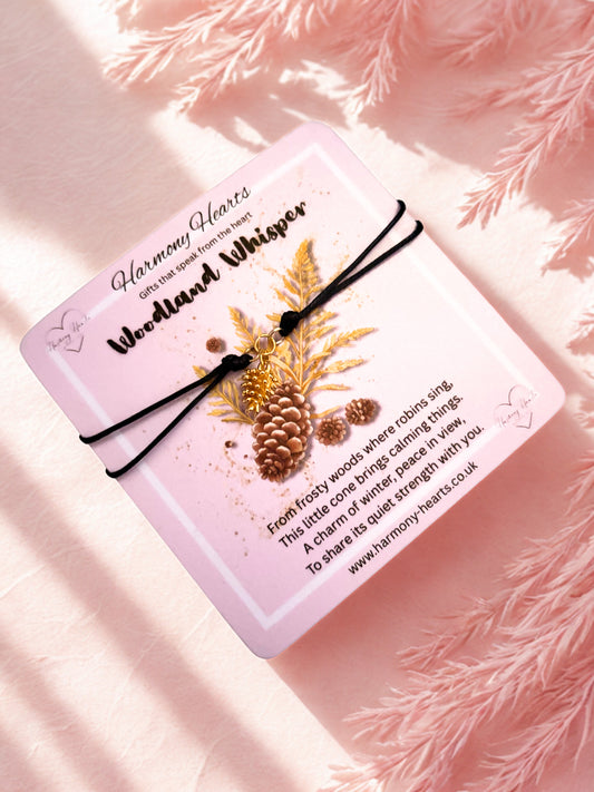 Pink card with nature-themed design and text on a pink textured background with a pine cone charm bracelet
