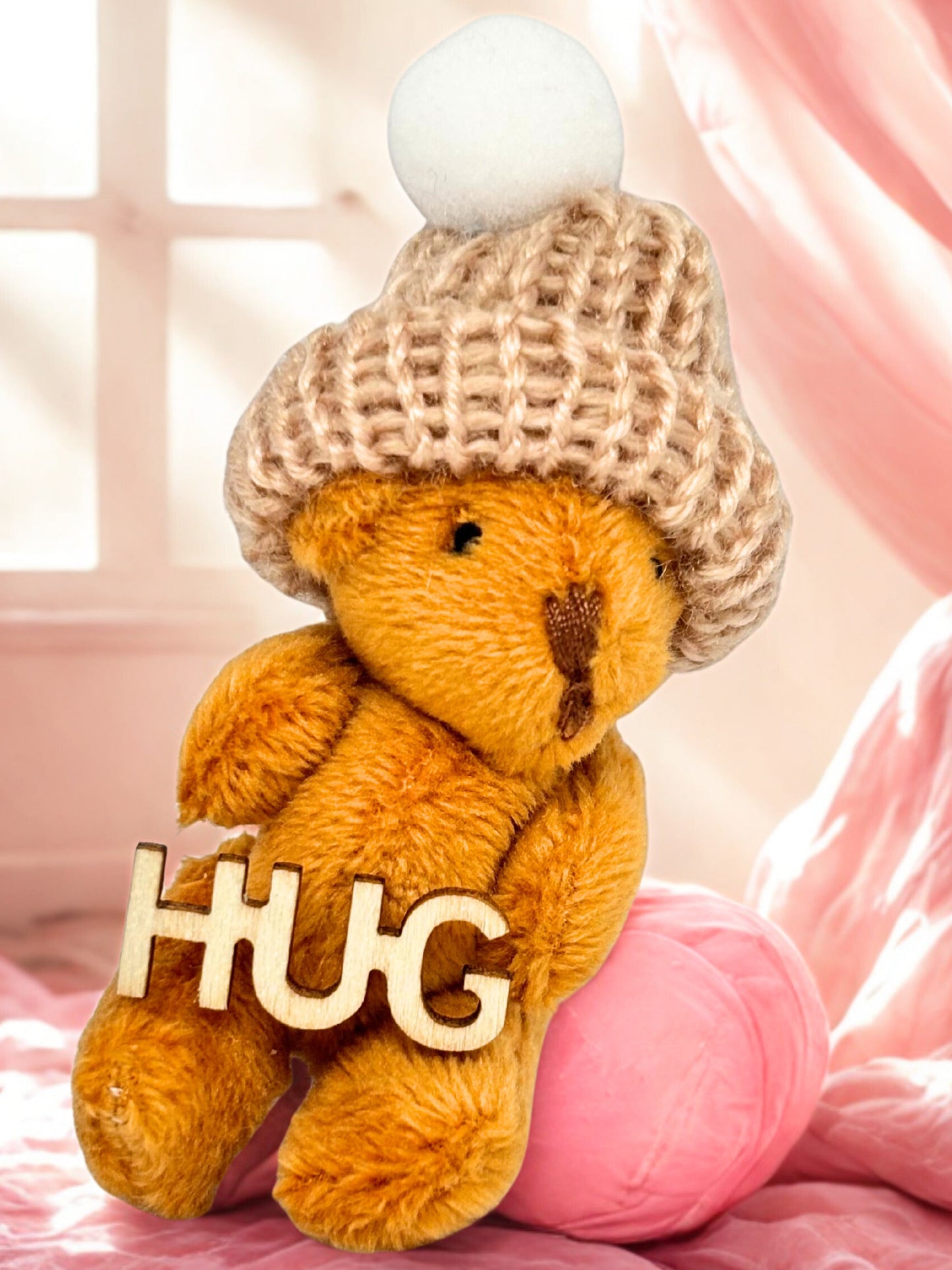 Teddy bear wearing a knitted hat with 'HUG' sign on pink blanket