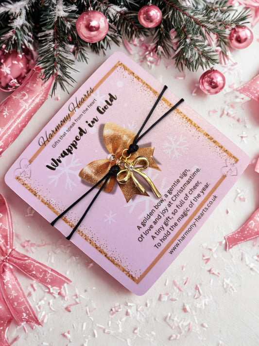 Pink card with gold bow and black charm bracelet with gold bow, surrounded by Christmas decorations.