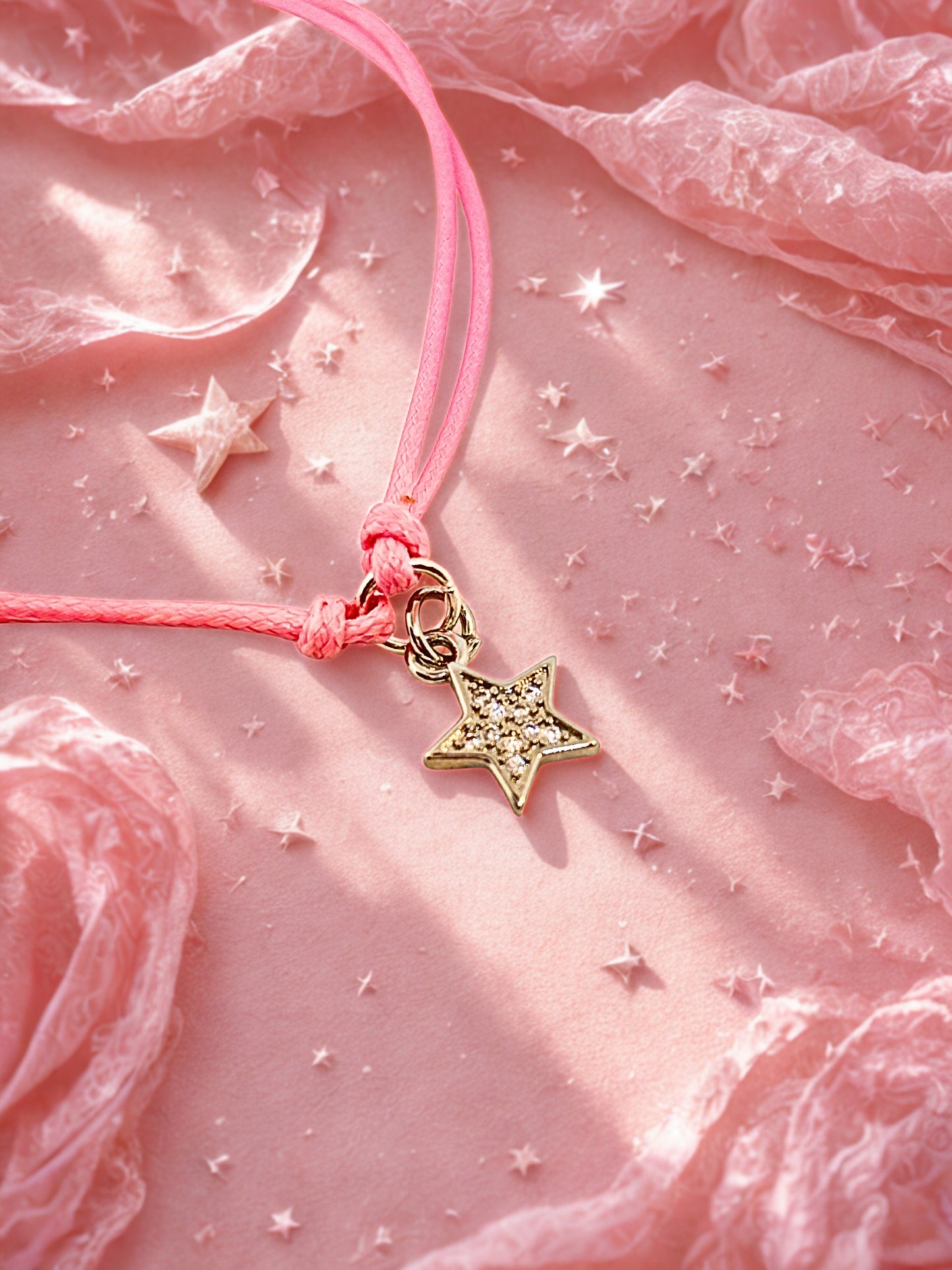 Pink cord bracelet with sparkly silver star charm on a soft pink surface