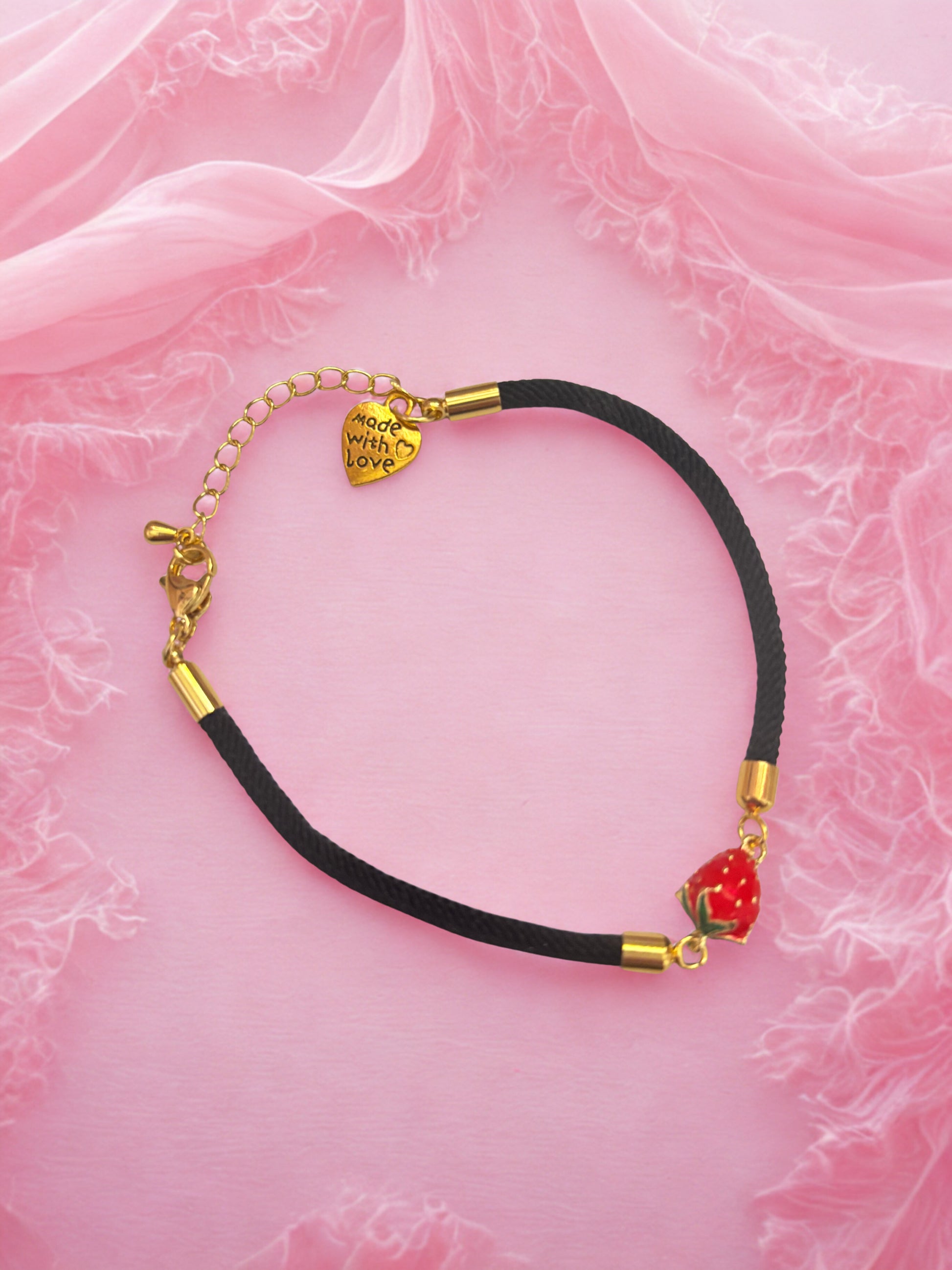 Bracelet with strawberry charm on a pink fabric background