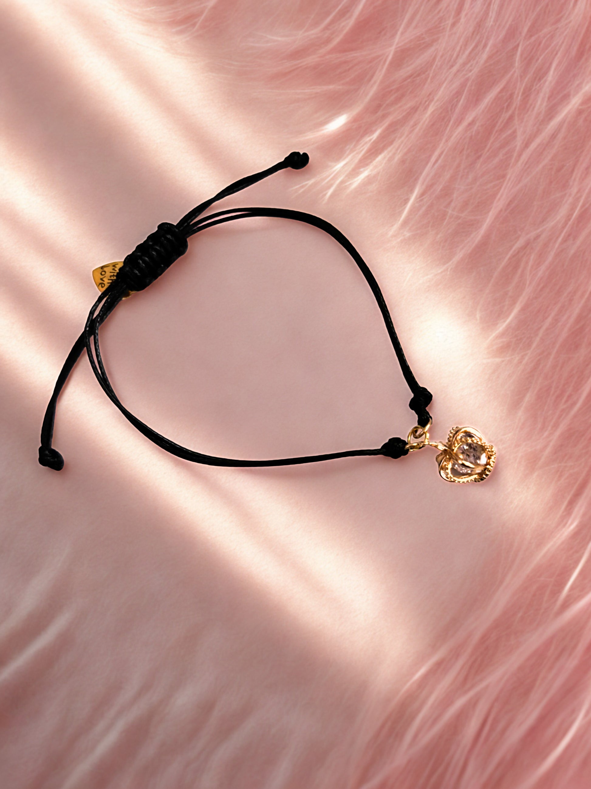 Black cord bracelet with gold crown charms on a pink fabric background
